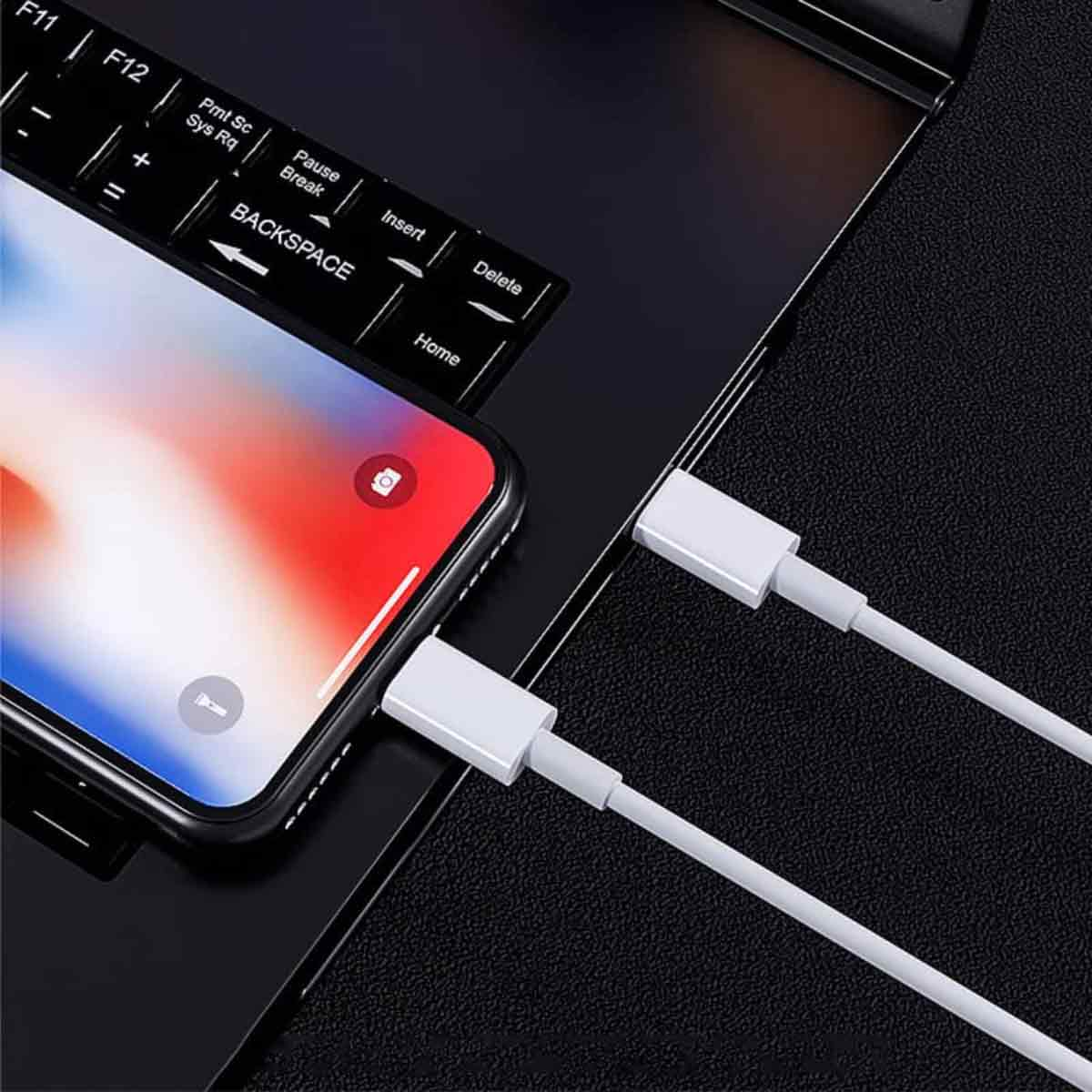 Ein Smartphone ist über weiße Ladekabel mit einem Laptop verbunden. Die Tastatur des Laptops und der Bildschirm des Telefons sind sichtbar.