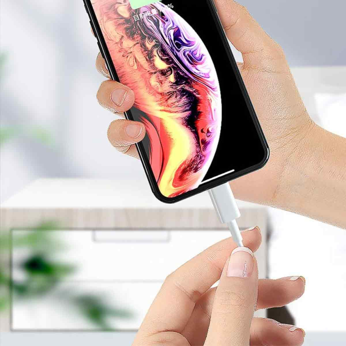Eine Hand hält ein Telefon, das mit einem weißen Kabel geladen wird. Der Bildschirm zeigt ein buntes Bild. Der Hintergrund ist unscharf.