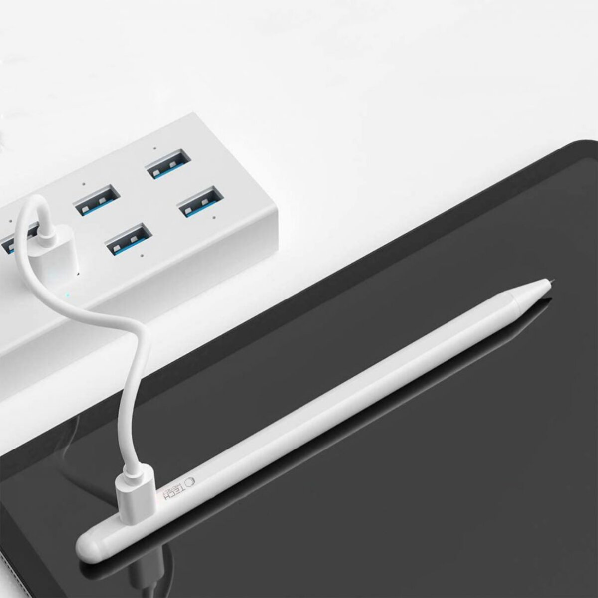 Weißer Stift und USB-Hub auf einem schwarzen Tablet. Der Hub hat 4 Anschlüsse. Ein weißes Kabel verbindet den Hub mit dem Tablet.