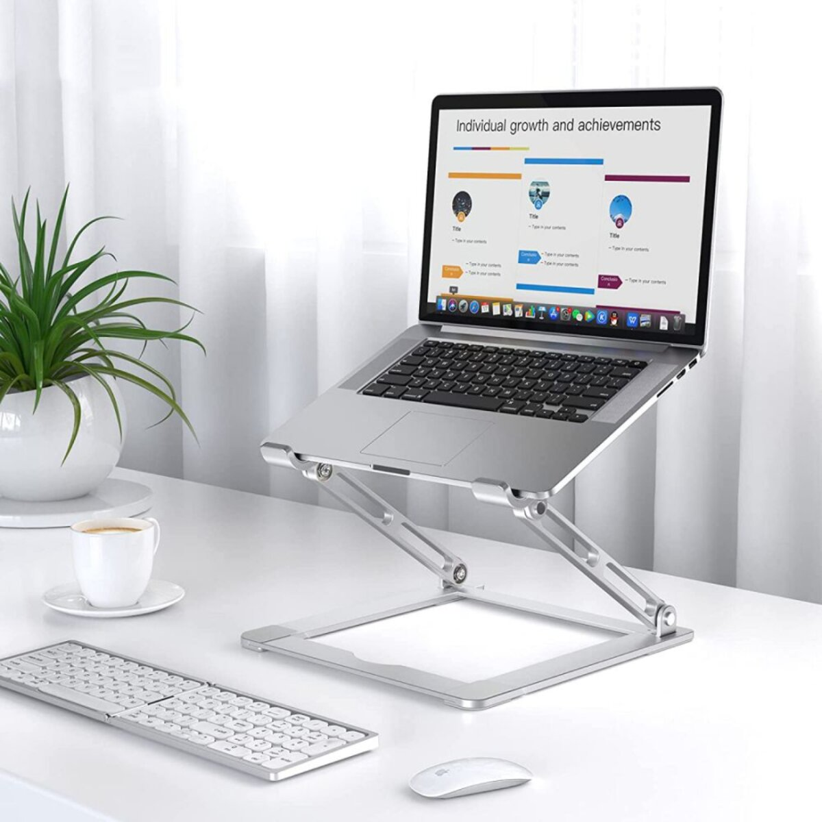 Laptop on a silver stand, keyboard, mouse, and a cup of coffee on a white desk. A plant is in the background.