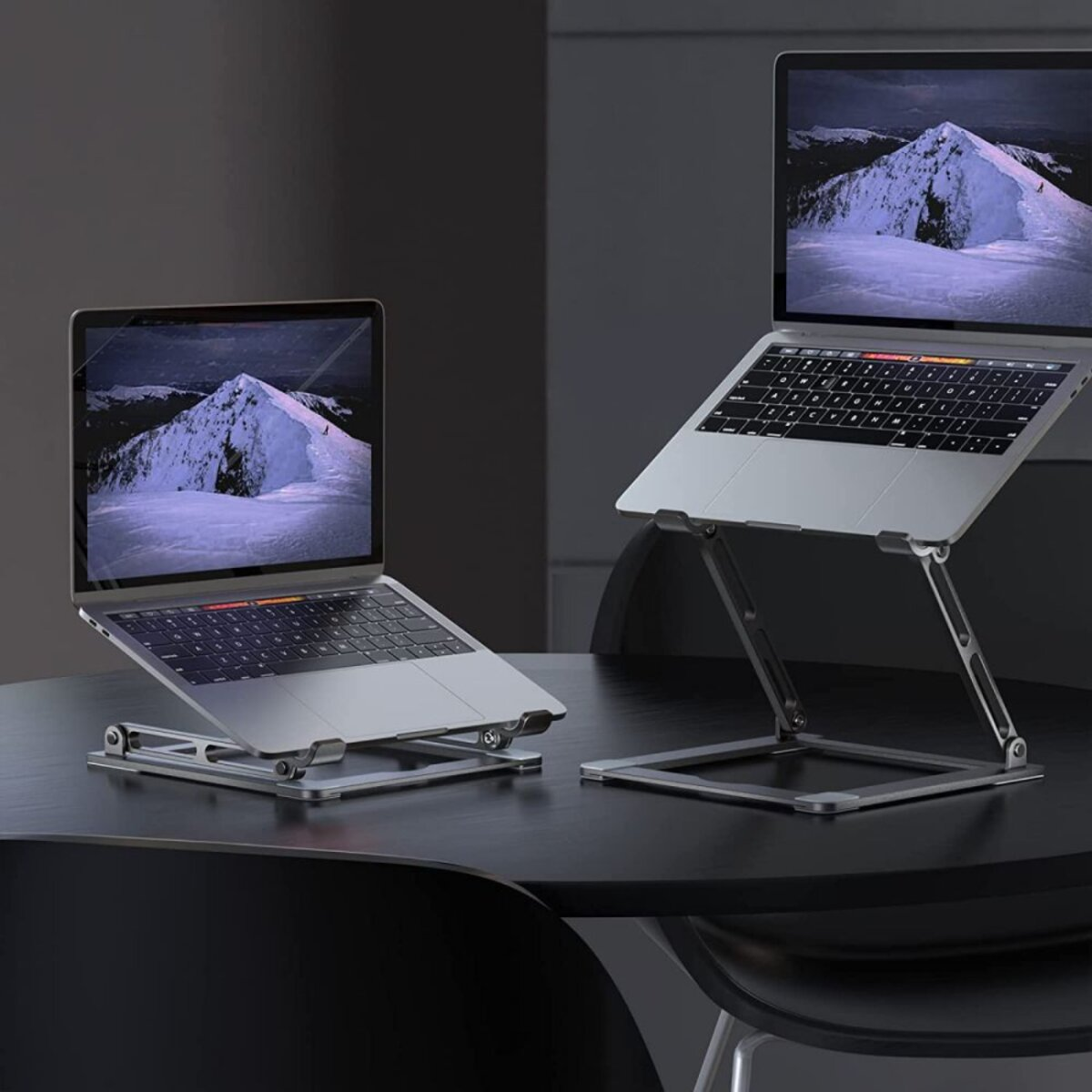 Two silver laptops on adjustable stands, displaying a snowy mountain scene on the screens, set on a dark table.