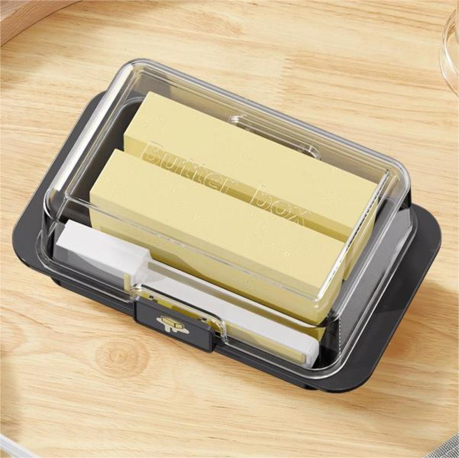 Butterdose mit Butter darin, auf einer Holzoberfläche. Die Dose hat einen durchsichtigen Deckel. Ein Buttermesser liegt daneben.