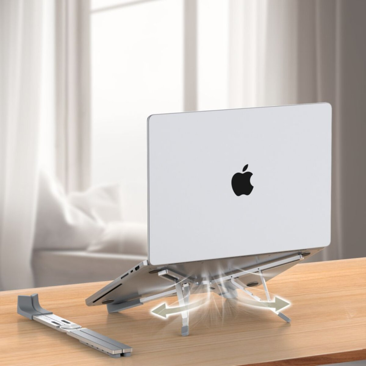 A silver laptop sits on a silver stand on a wooden table. An additional stand piece lies beside it. A window is in the background.