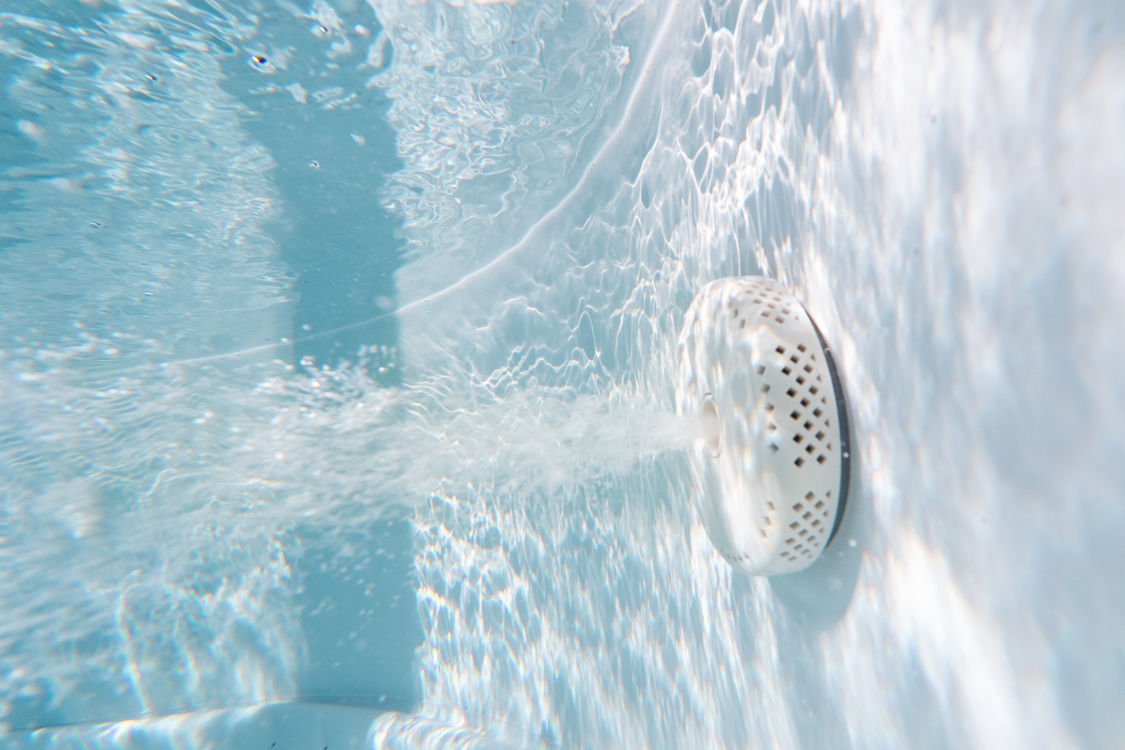 Unterwasseransicht eines Pools. Ein weißer Wasserstrahl stößt Wasser aus. Das Wasser ist klar, mit Lichtreflexen und Blasen.