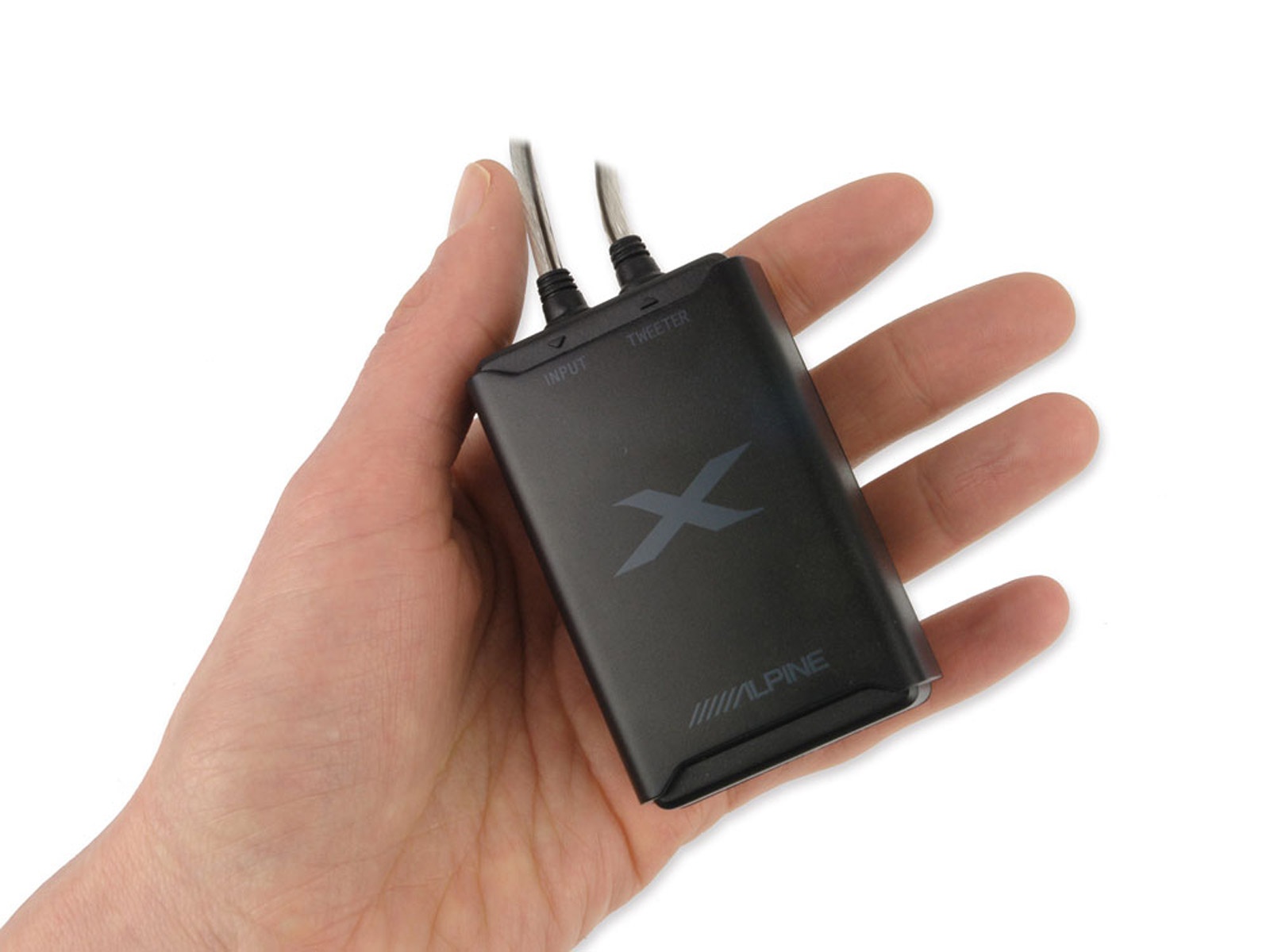 Eine Hand hält ein schwarzes Alpine-Gerät mit Eingangs- und Hochtöneranschlüssen. Es hat ein X-Logo.
