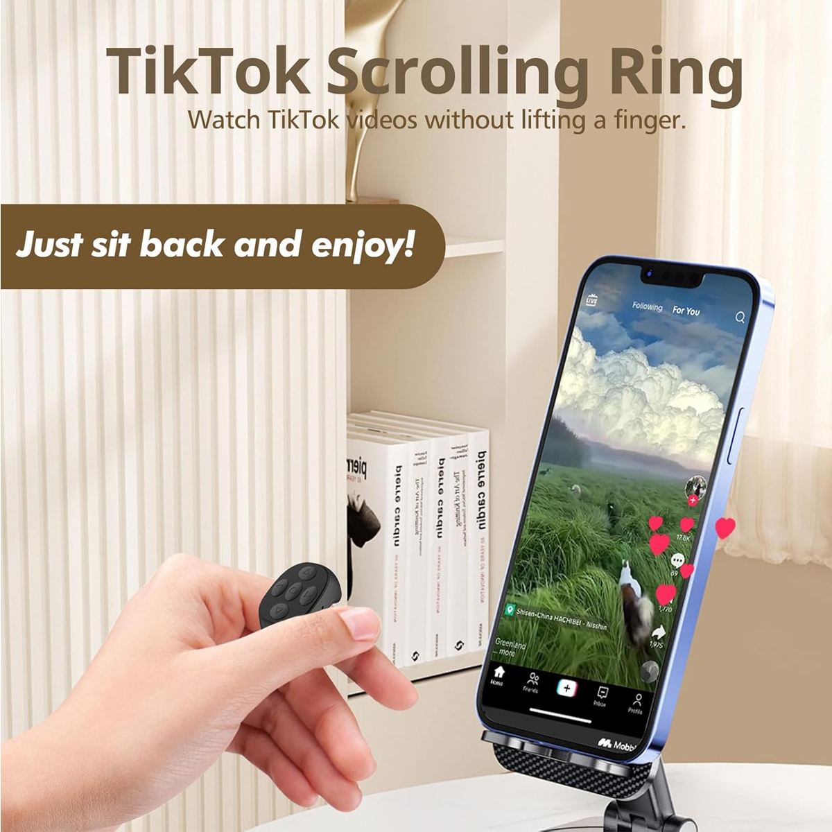 Ein Telefon mit einem TikTok-Video wird von einem Ständer gehalten. Eine Hand hält eine Fernbedienung. Bücher und ein weißer Schrank im Hintergrund.