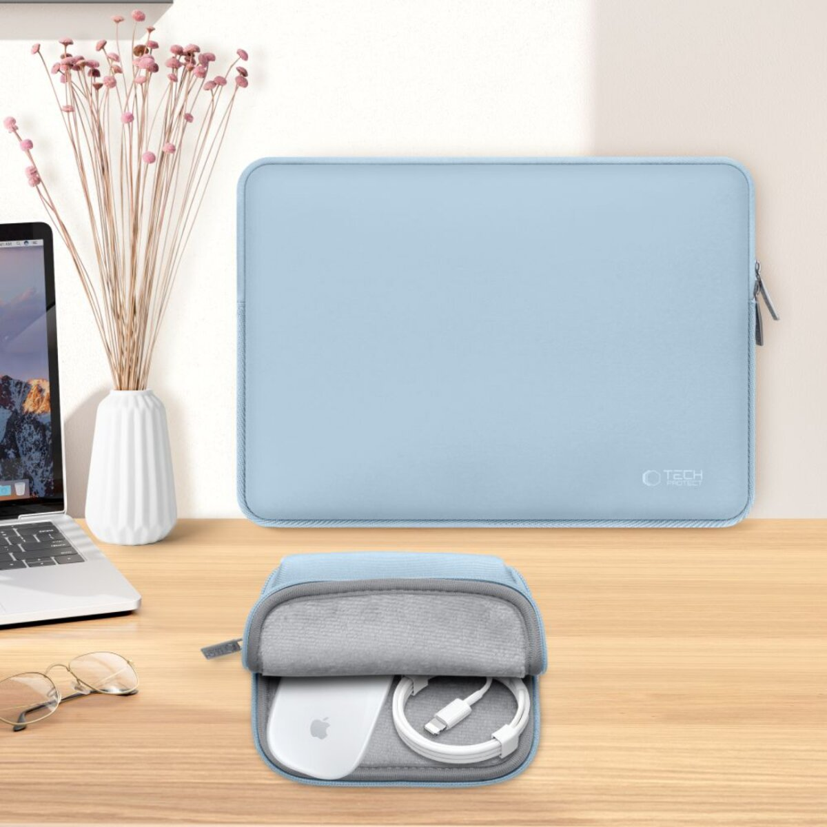 Een lichtblauwe laptoptas, een kleinere etui met een muis en kabel, een vaas met bloemen en een laptop op een houten oppervlak.