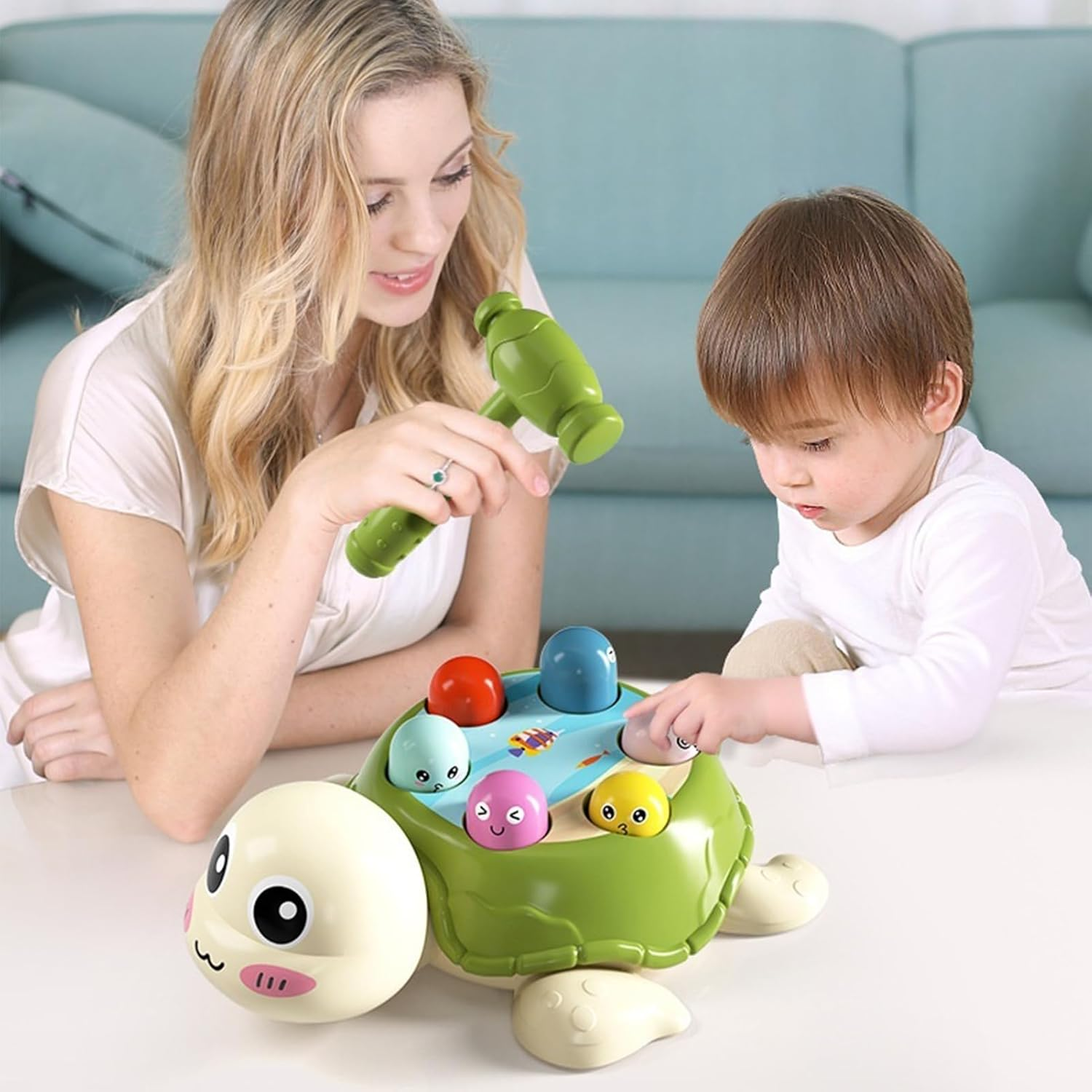 Eine Frau und ein Kind spielen mit einem schildkrötenförmigen Spielzeug. Das Spielzeug hat bunte Bälle und einen Hammer. Im Hintergrund ist ein Sofa.