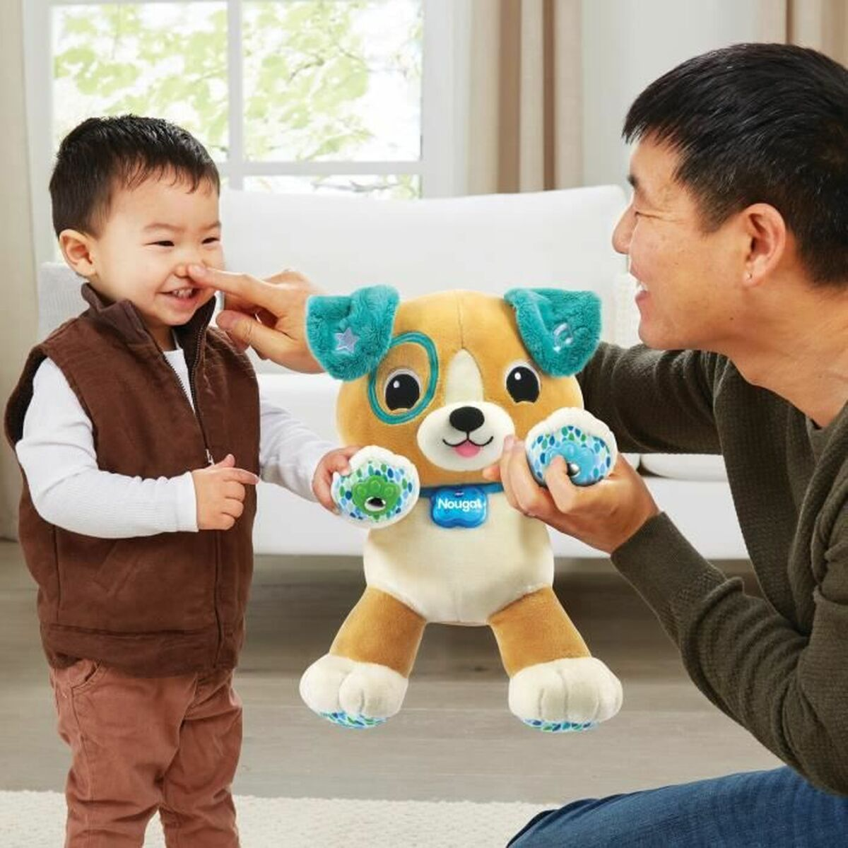 Ein Mann und ein Kleinkind spielen mit einem Plüschhundespielzeug. Der Junge lächelt. Das Spielzeug hat blaue Akzente.