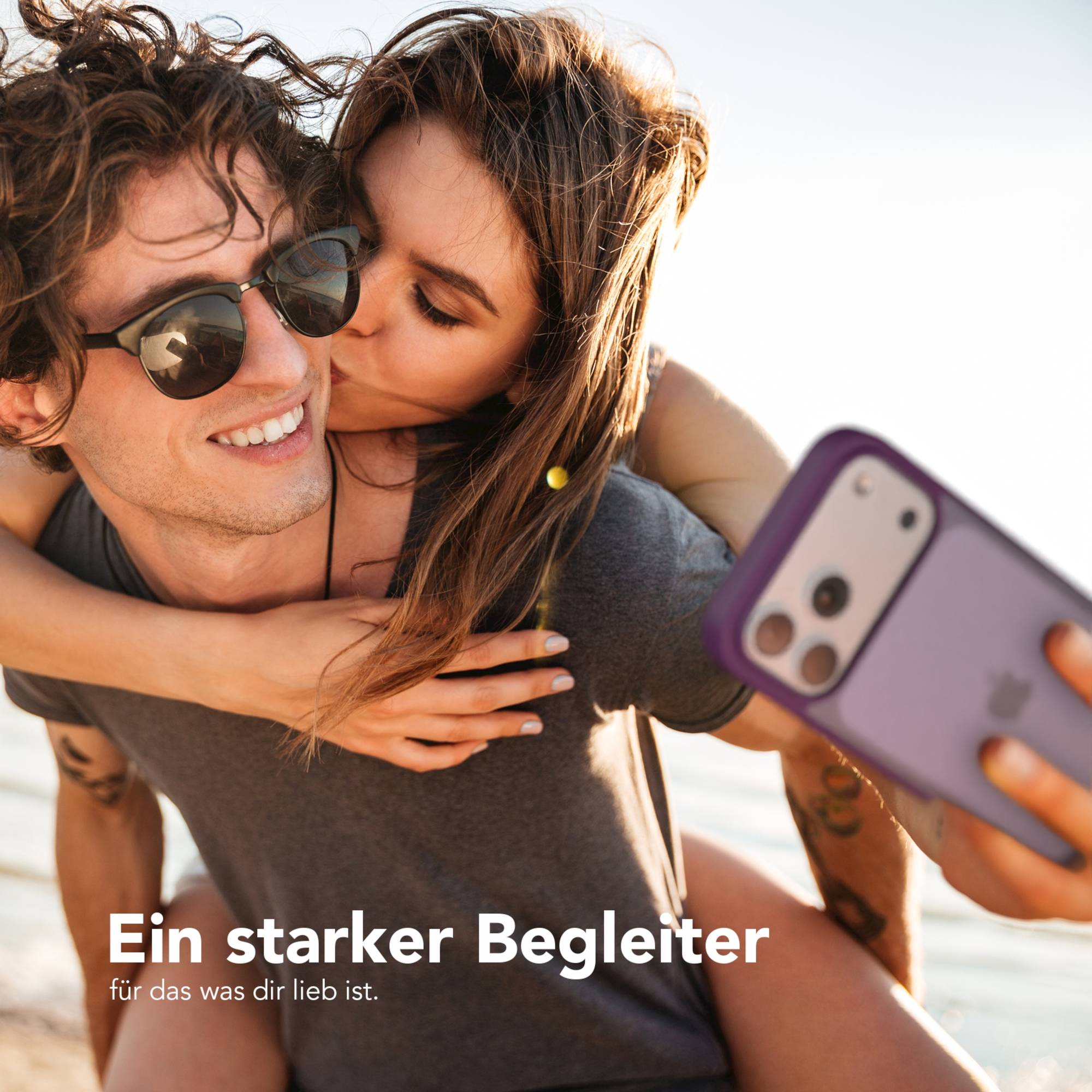 Eine Frau küsst einen Mann auf die Wange. Er trägt eine Sonnenbrille. Sie halten ein Telefon. Text: Ein starker Begleiter.