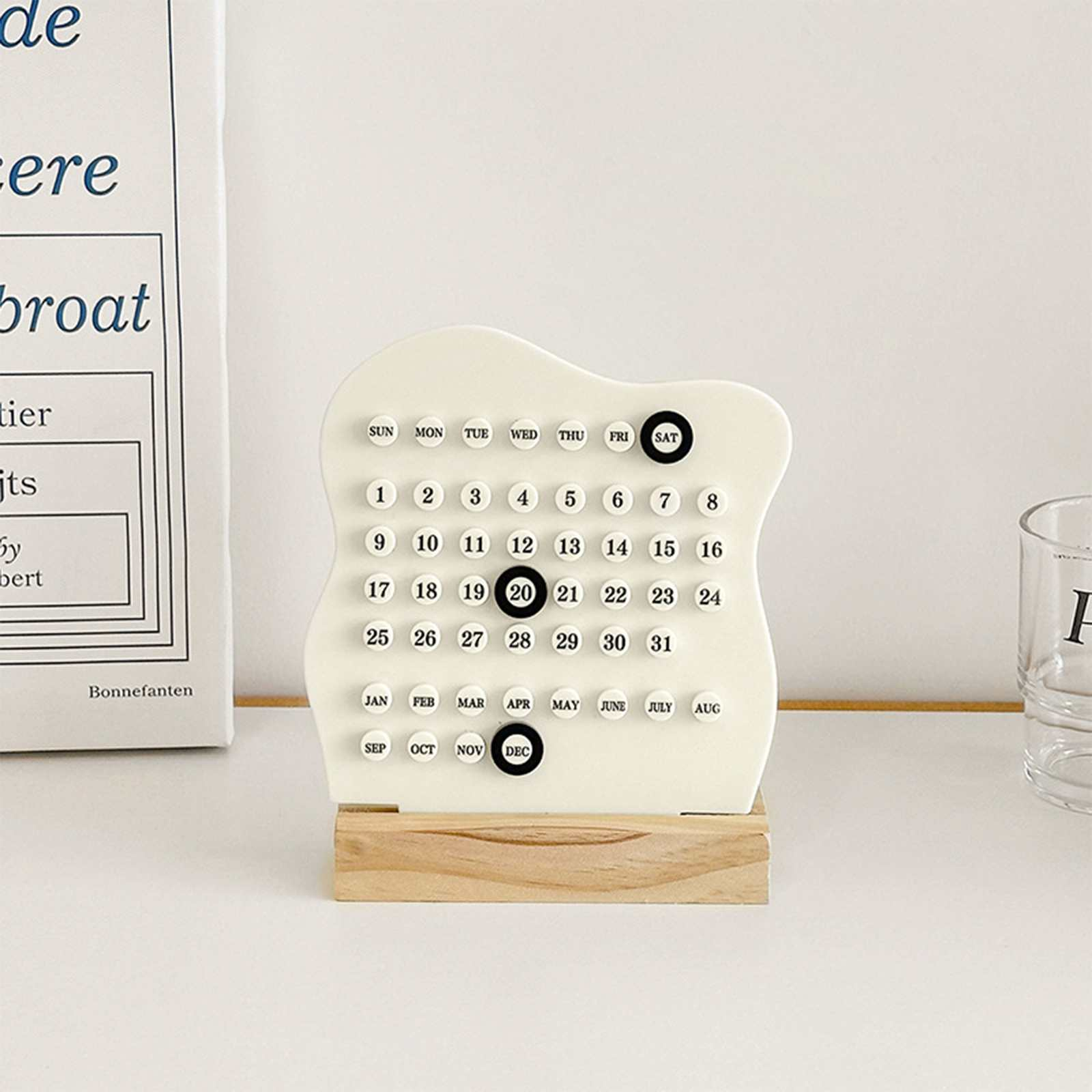 Ein cremefarbener Kalender mit schwarzen Zahlen steht auf einem Holzsockel. Das aktuelle Datum, der 20. Dezember, ist hervorgehoben.