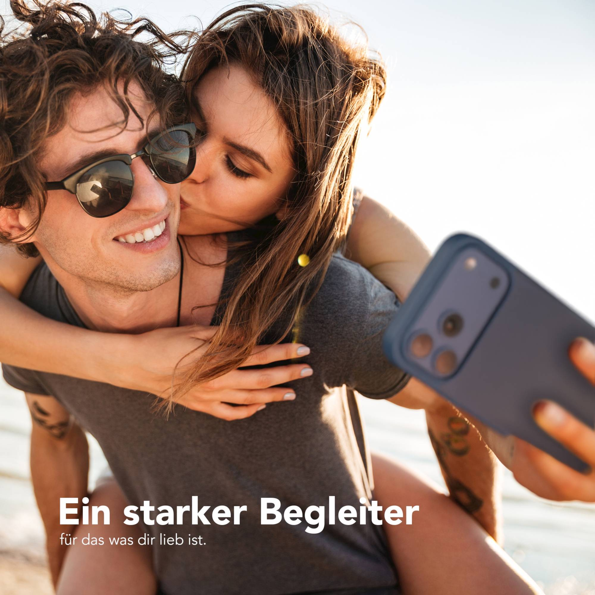 Ein Paar macht ein Selfie. Die Frau küsst die Wange des Mannes, während er das Telefon hält. Sie lächeln.