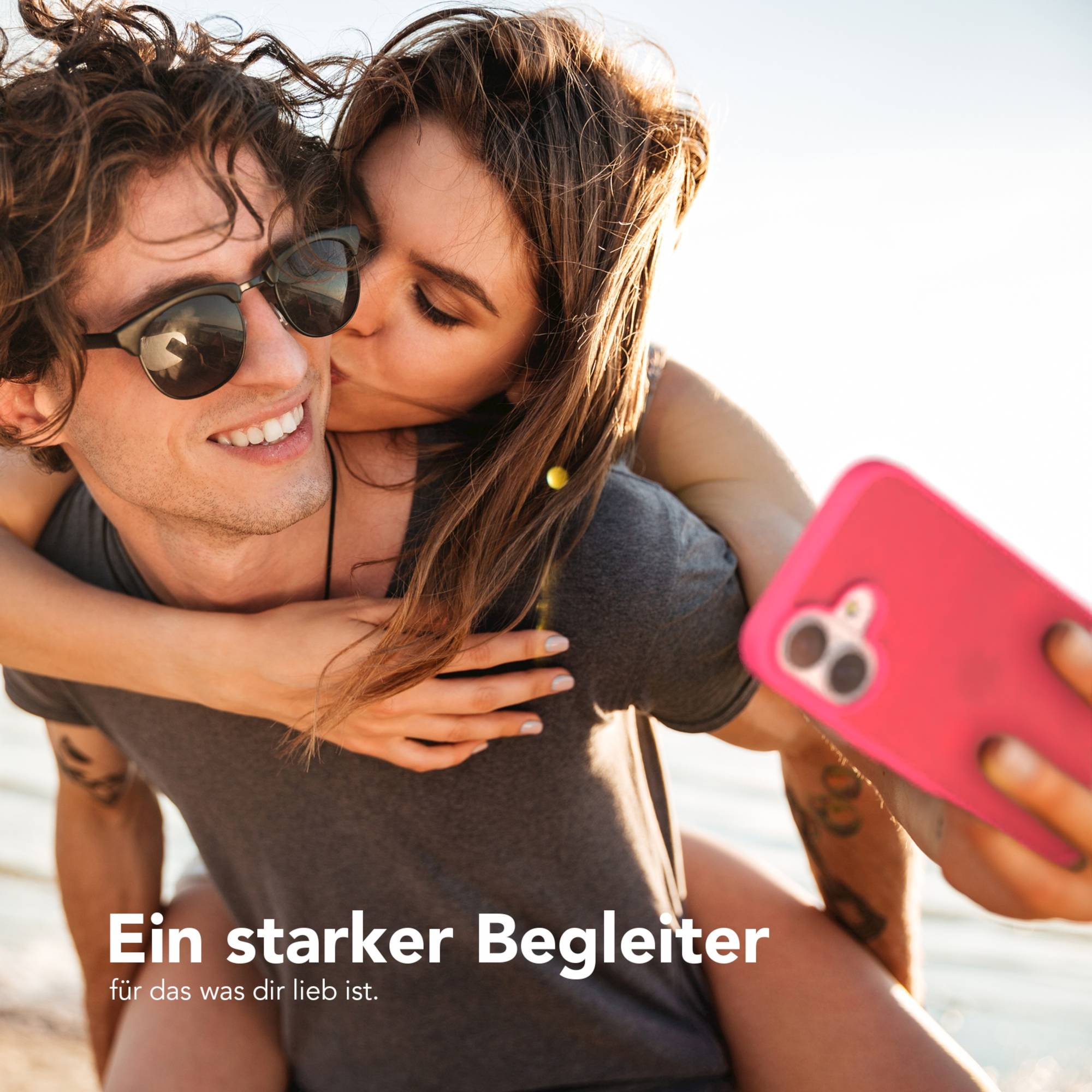 Eine Frau küsst einen Mann auf die Wange, während er ein Telefon hält. Sie sind draußen. Das Telefon hat eine pinke Hülle.