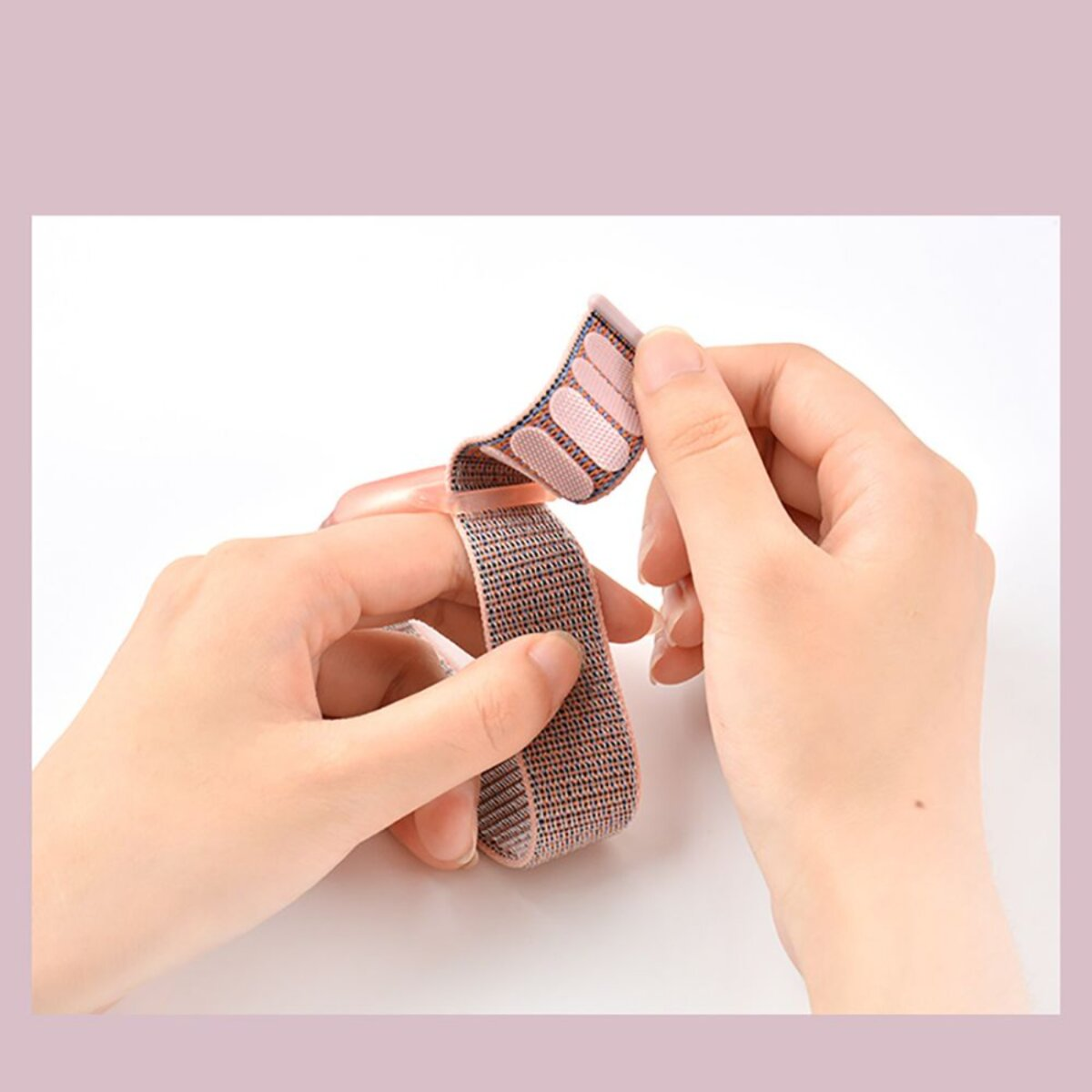 Hände passen ein Armband an. Das Band ist beige und rosa, mit Klettverschluss. Der Hintergrund ist weiß mit einem rosa Rand.