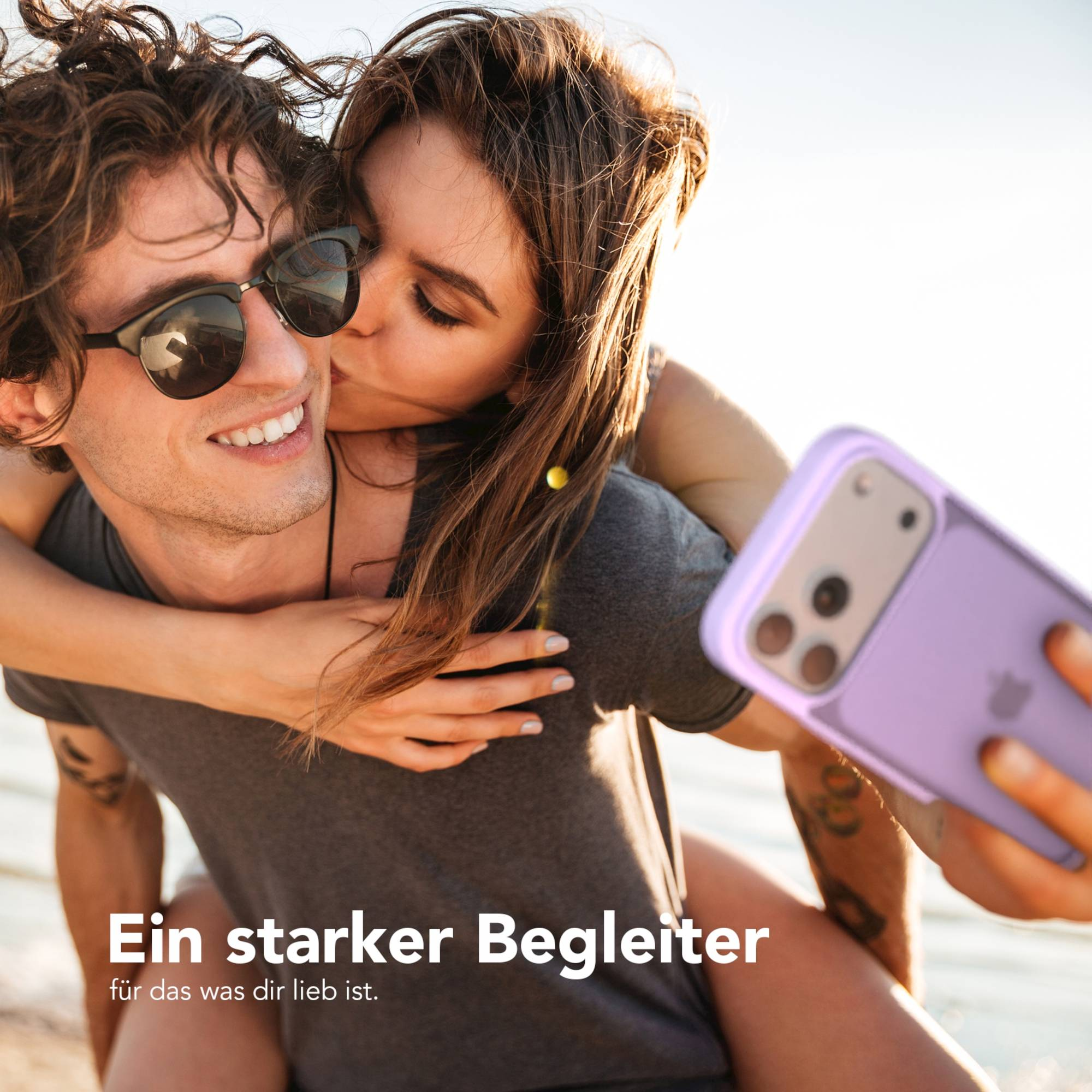 Ein Paar macht ein Selfie mit einem Telefon. Die Frau küsst die Wange des Mannes. Das Telefon hat eine lila Hülle.