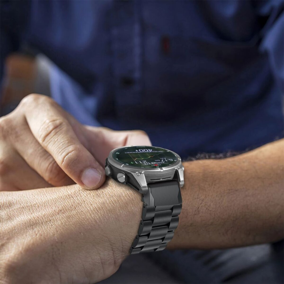 Una persona indossa uno smartwatch argento e nero. L'orologio visualizza dati. Sono visibili il braccio della persona e una camicia blu.