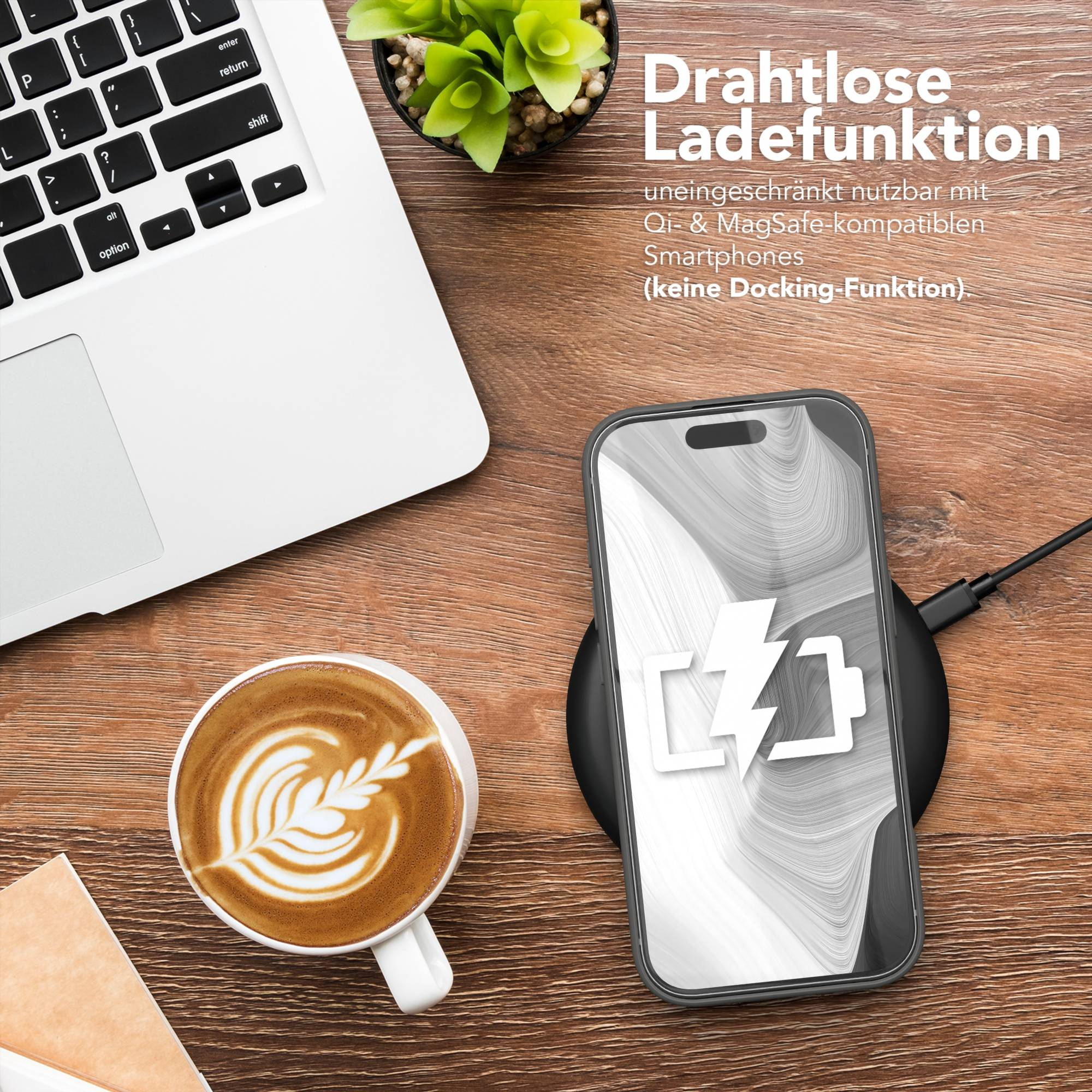 Laptop, Kaffee, Telefon auf Ladegerät und kleine Pflanze auf einem Holztisch. Telefon zeigt Ladesymbol.
