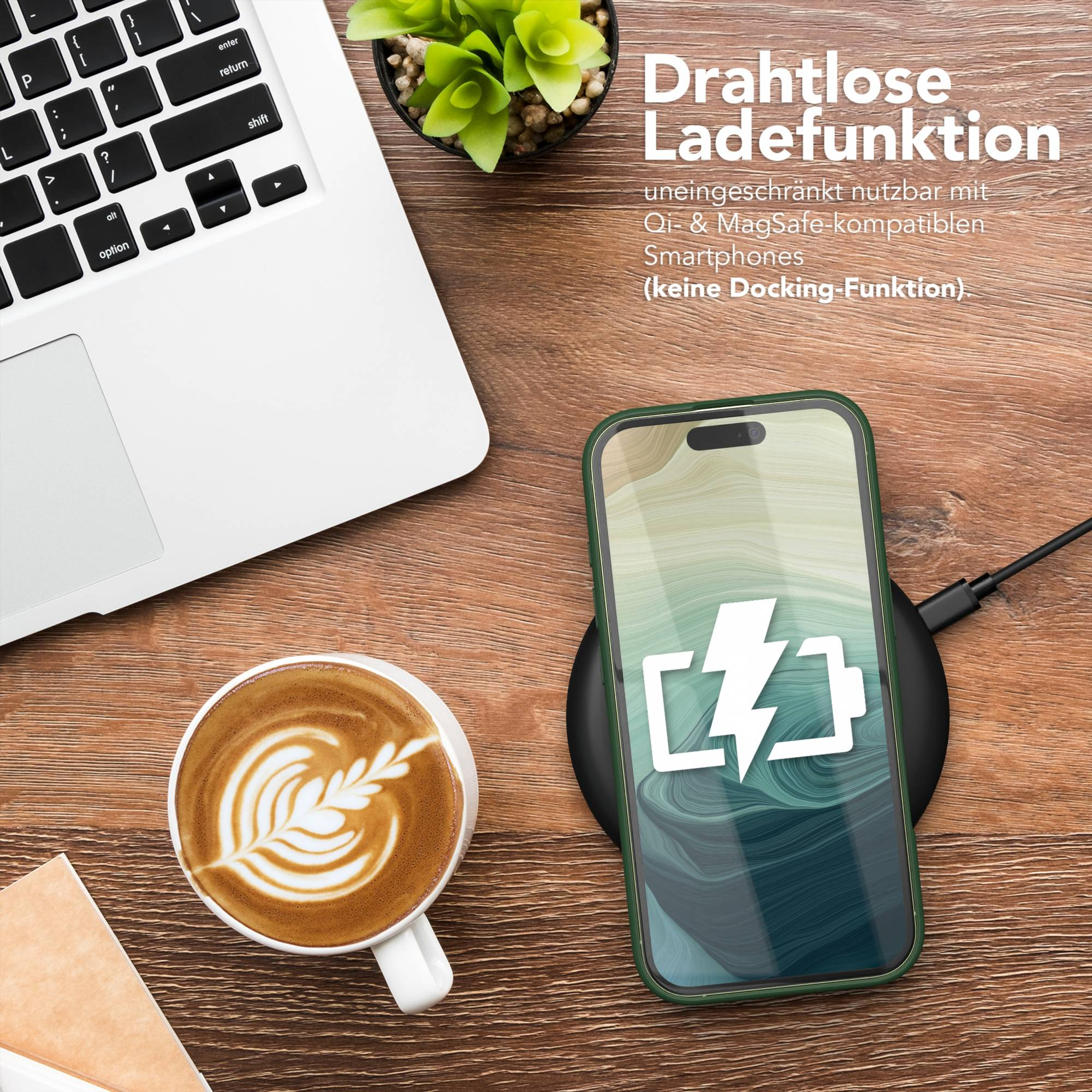 Telefon auf Ladegerät, Kaffee, Laptop auf Holzoberfläche. Telefon zeigt Akkusymbol. Pflanze im Topf.