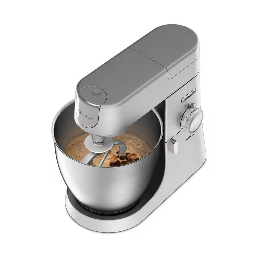 Srebrny mikser Kenwood Chef XL z misą zawierającą ciasto i kawałki czekolady. Mikser stoi na białej powierzchni.