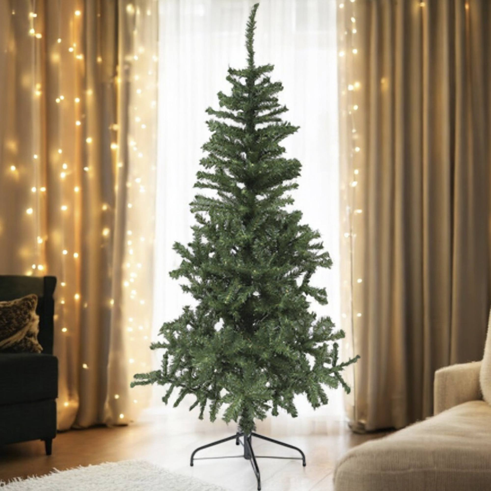 Un árbol de Navidad artificial verde está frente a una ventana. Cortinas y luces de hadas en el fondo.