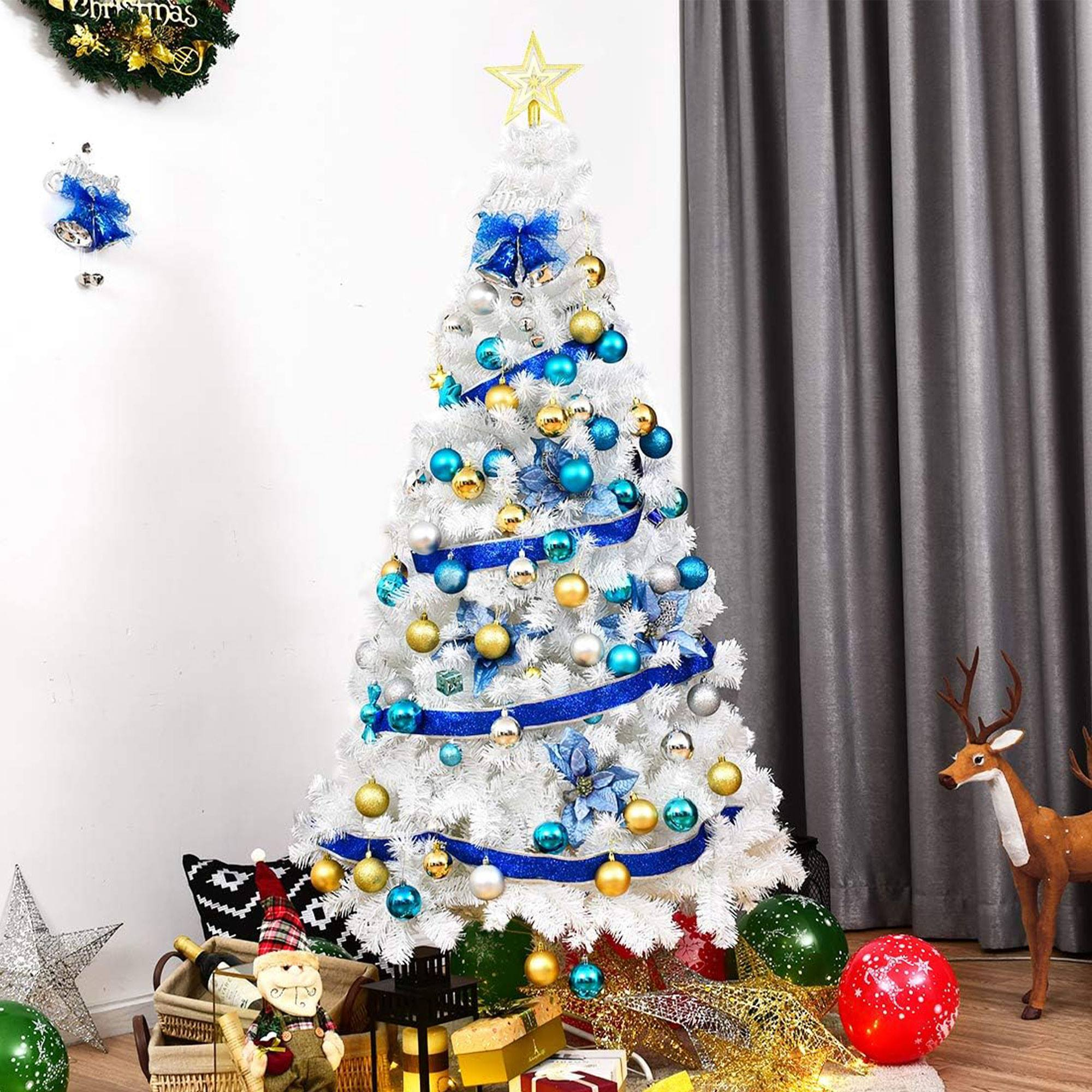 Un árbol de Navidad blanco con adornos azules y dorados, coronado por una estrella. Un reno y regalos en la base.