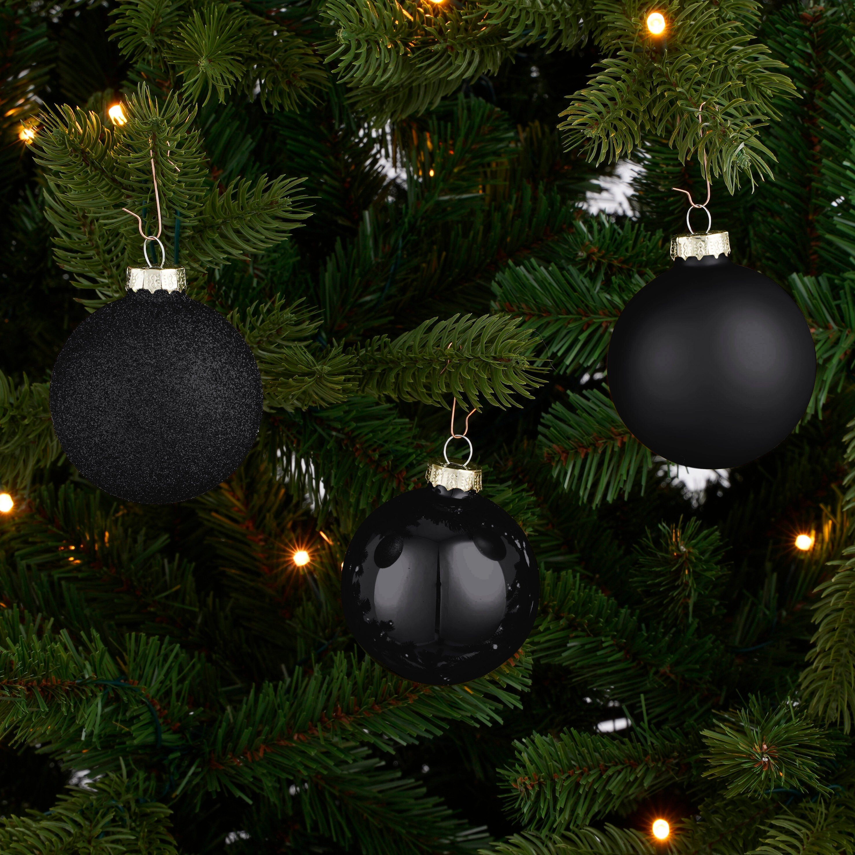 Gros plan sur un sapin de Noël avec trois ornements noirs. L'arbre a des aiguilles vertes et quelques petites lumières.