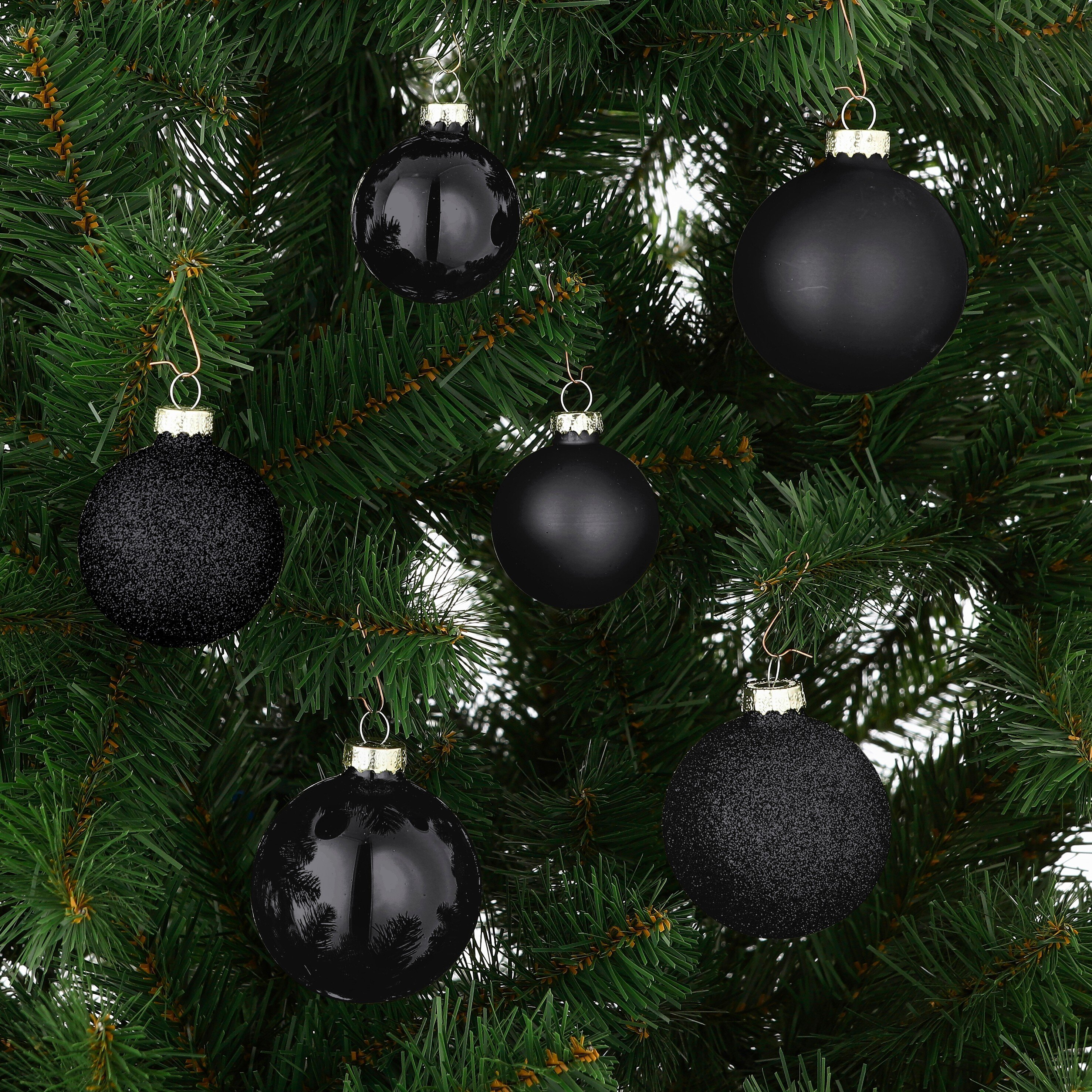 Gros plan sur un sapin de Noël décoré de multiples ornements noirs de textures différentes.