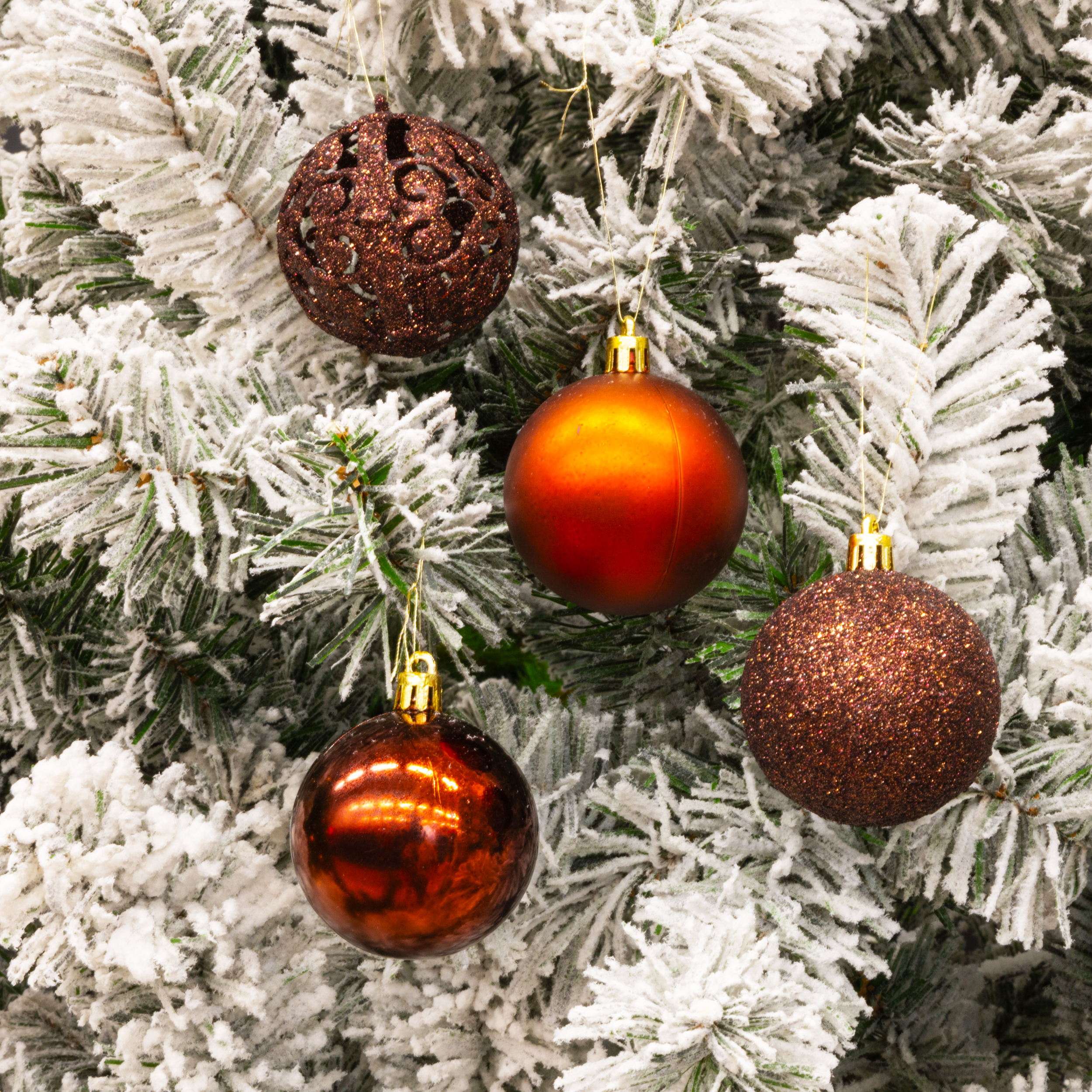 Gros plan d'un sapin de Noël avec des ornements bruns et des branches enneigées. Quatre ornements sont visibles.