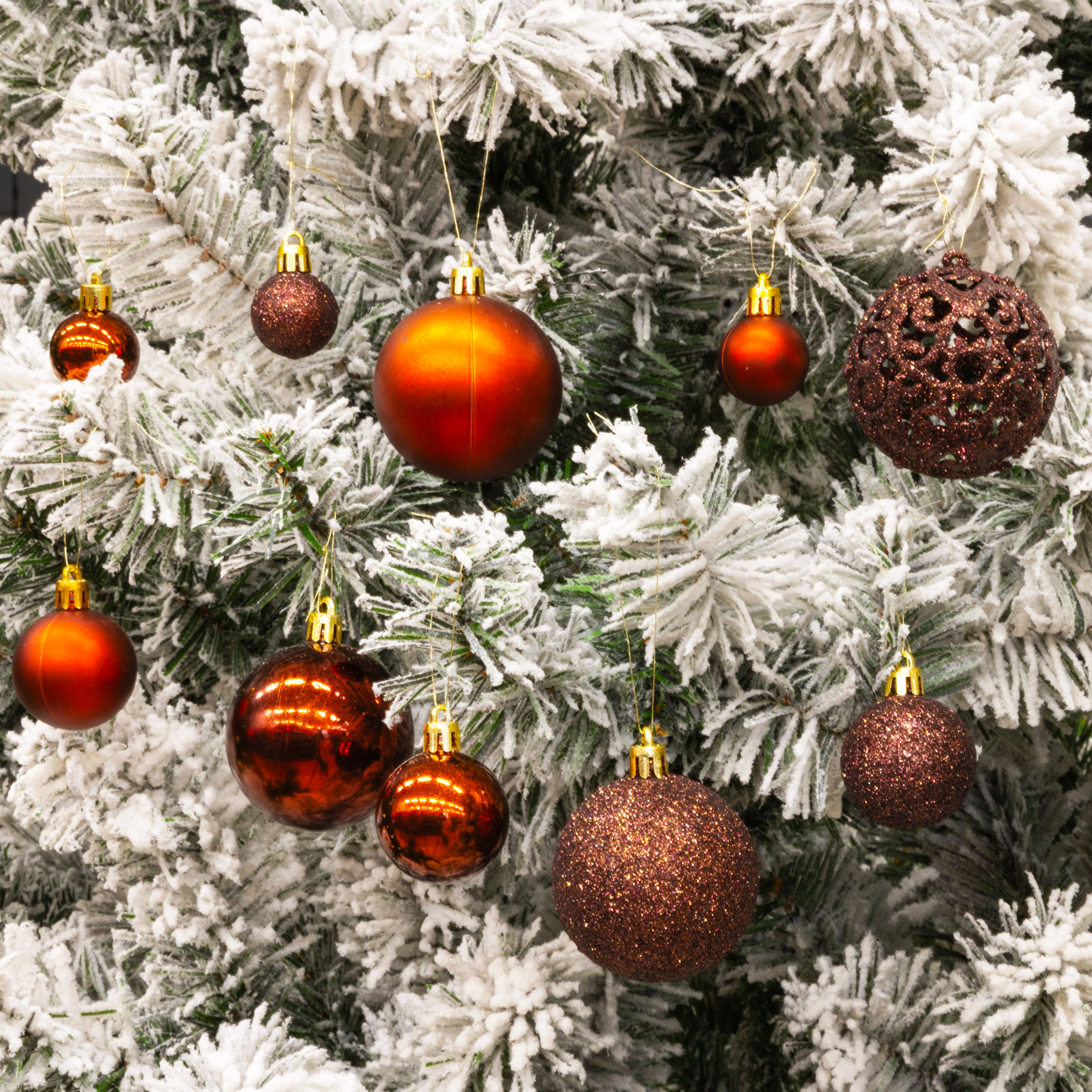 Gros plan d'un sapin de Noël orné de décorations rouges et marron, recouvert de neige artificielle.