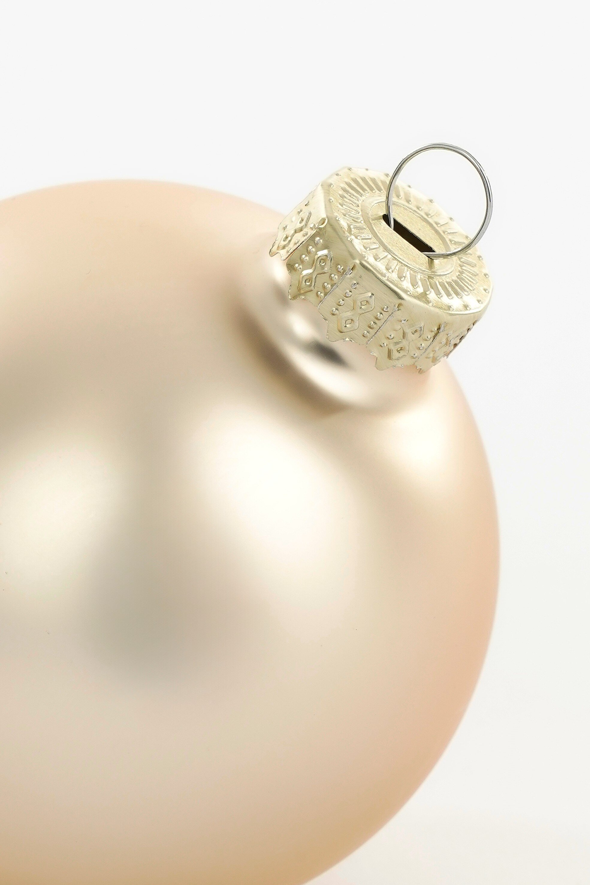 Gros plan d'une boule de Noël beige avec anneau supérieur argenté, sur fond blanc.