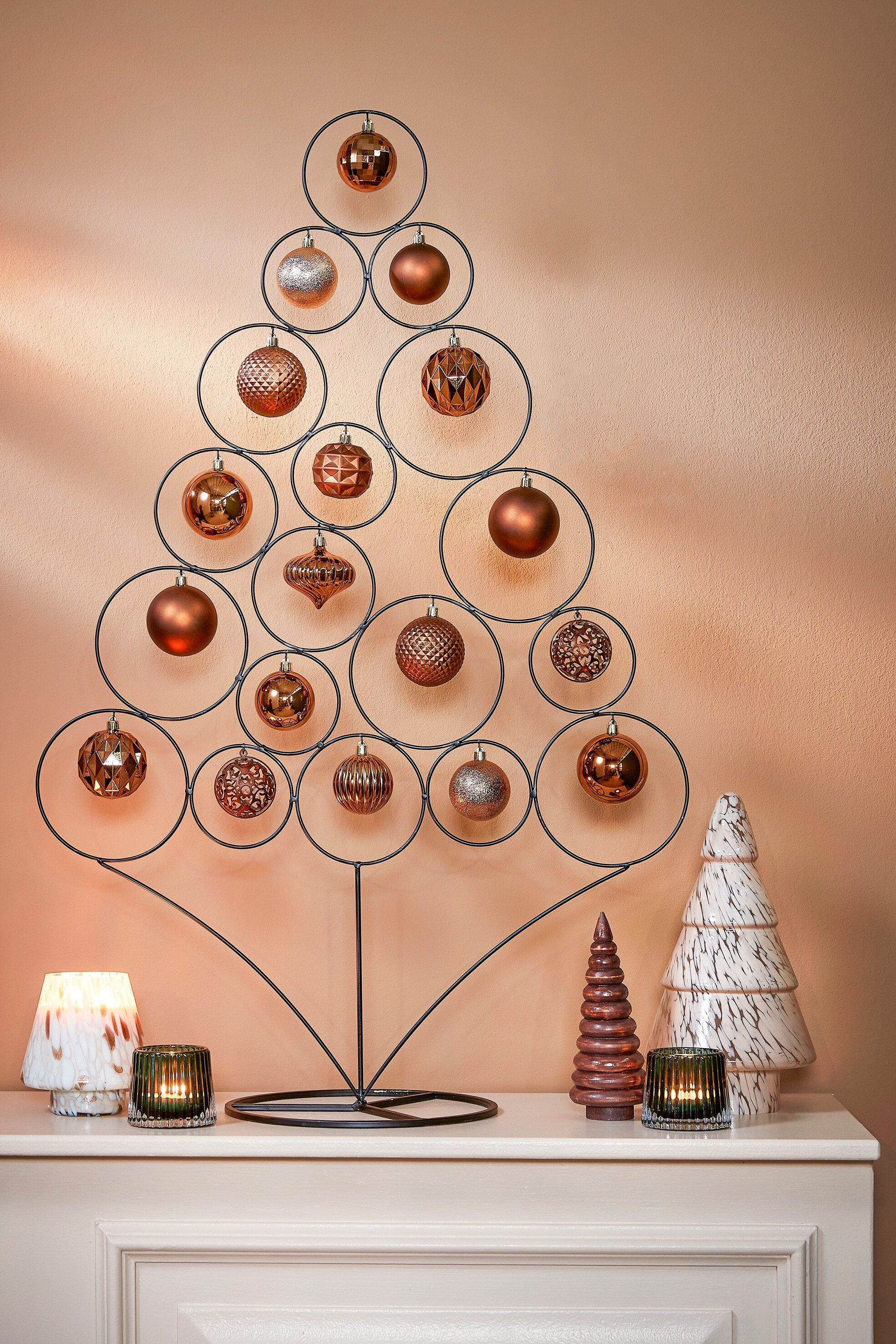 Un sapin de Noël en métal avec des ornements. Des bougies et des arbres décoratifs sur une cheminée blanche.