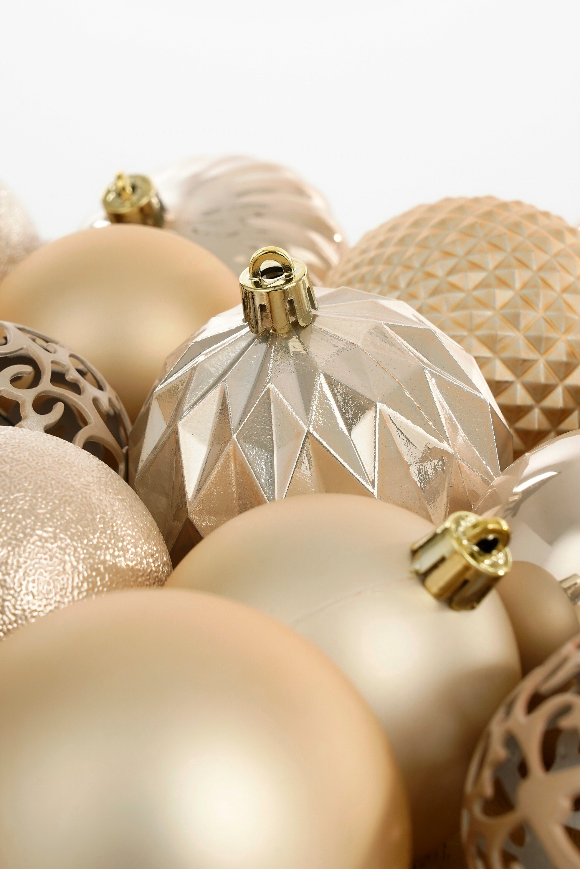Gros plan de diverses décorations de Noël dorées et argentées, certaines à motifs. Fond blanc.