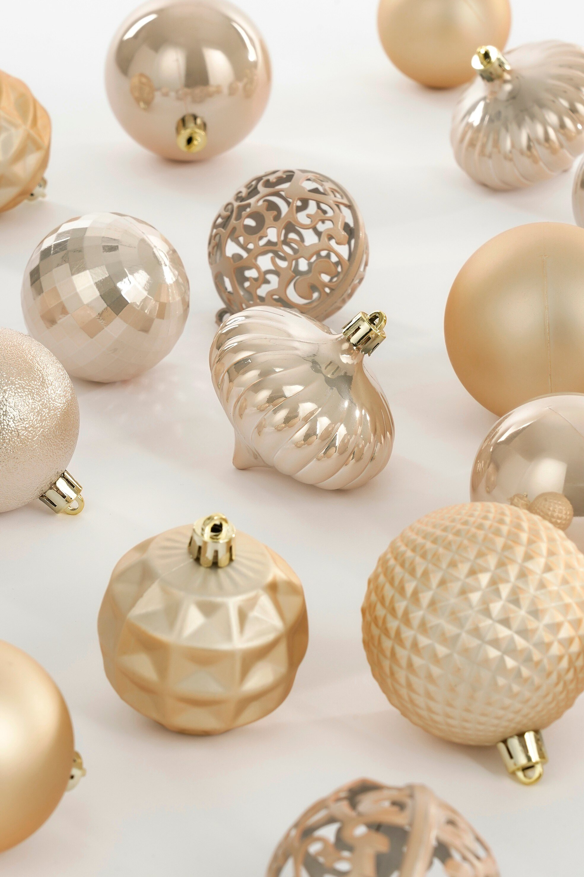 Diverses boules de Noël dorées sur une surface blanche. Certaines sont rondes, d'autres texturées.