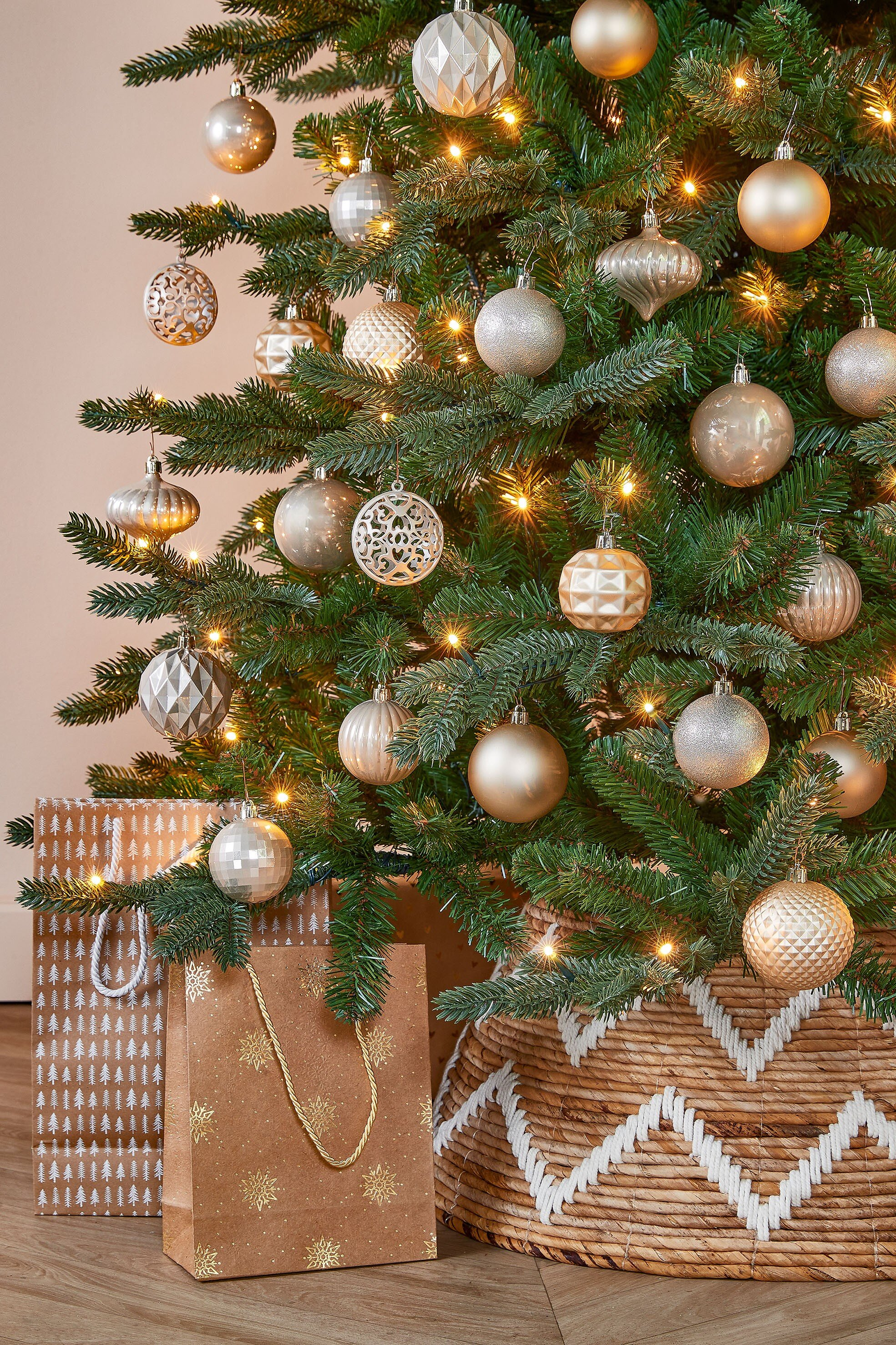 Un sapin de Noël décoré avec des ornements, des lumières et des sacs cadeaux. Un panier en osier entoure la base.