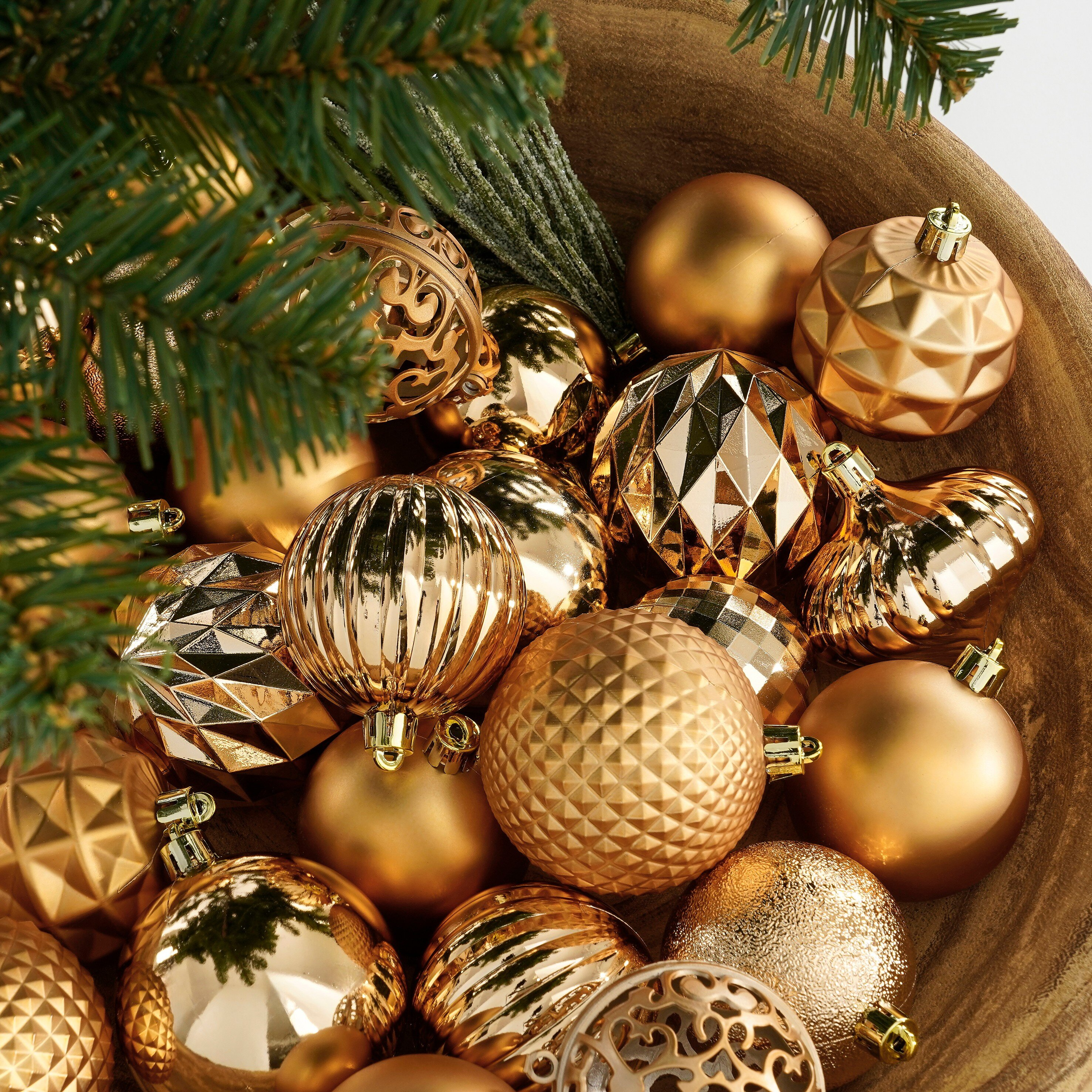 Gouden kerstversiering in een houten kom, met groene dennentakken. Verscheidenheid aan texturen en vormen.