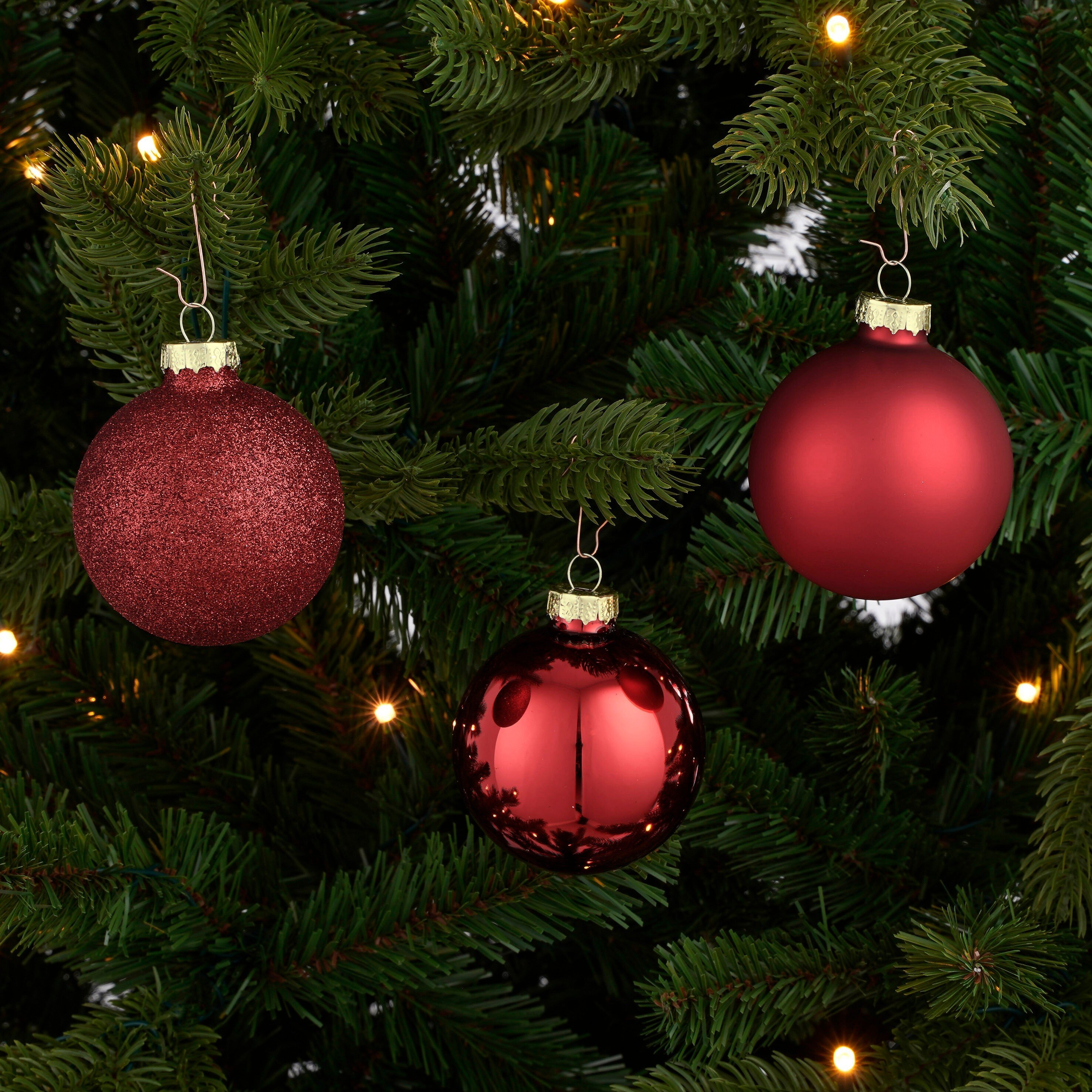 Gros plan d'un sapin de Noël avec trois ornements rouges et des lumières.
