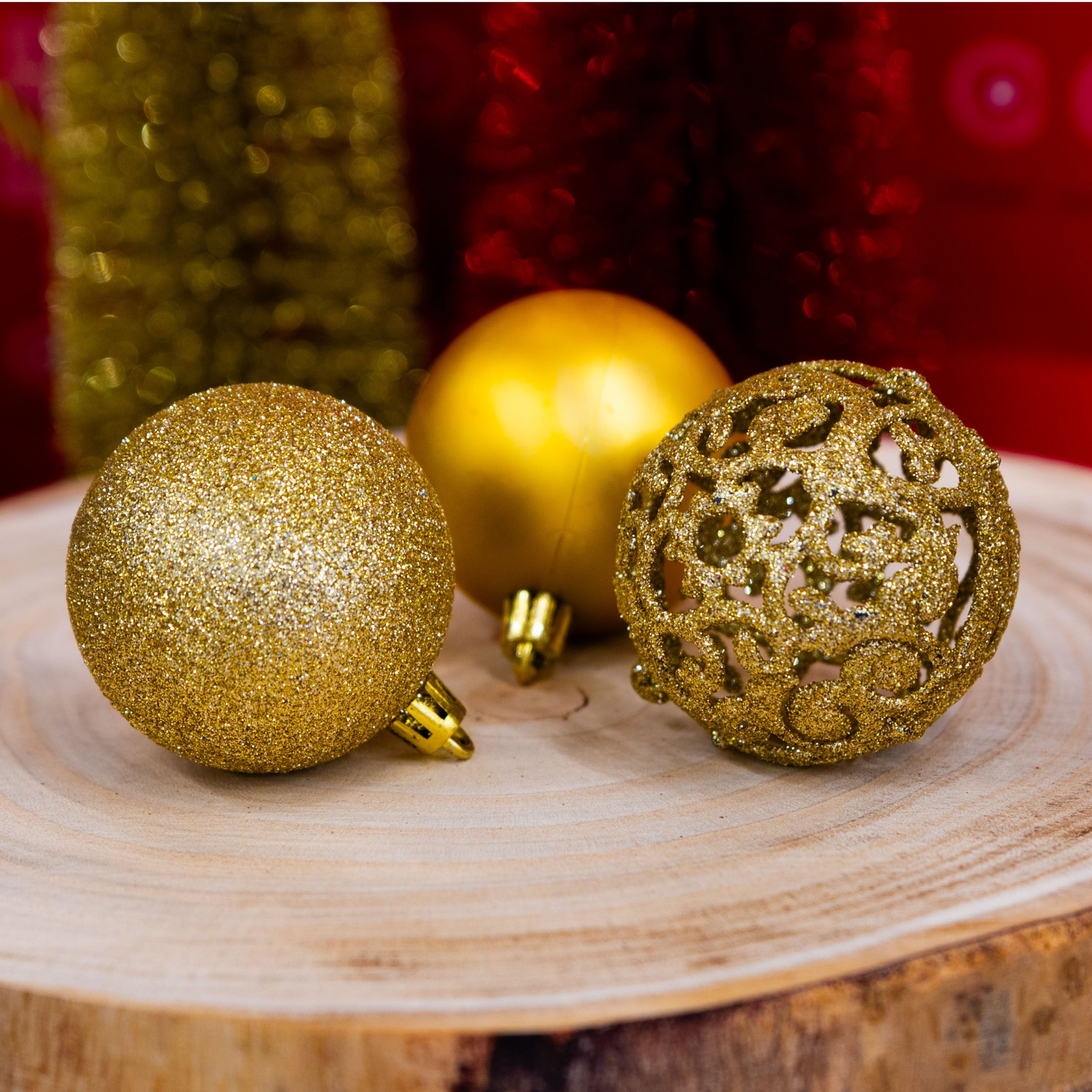 Trois boules de Noël dorées sur une surface en bois, avec un fond flou rouge et or.