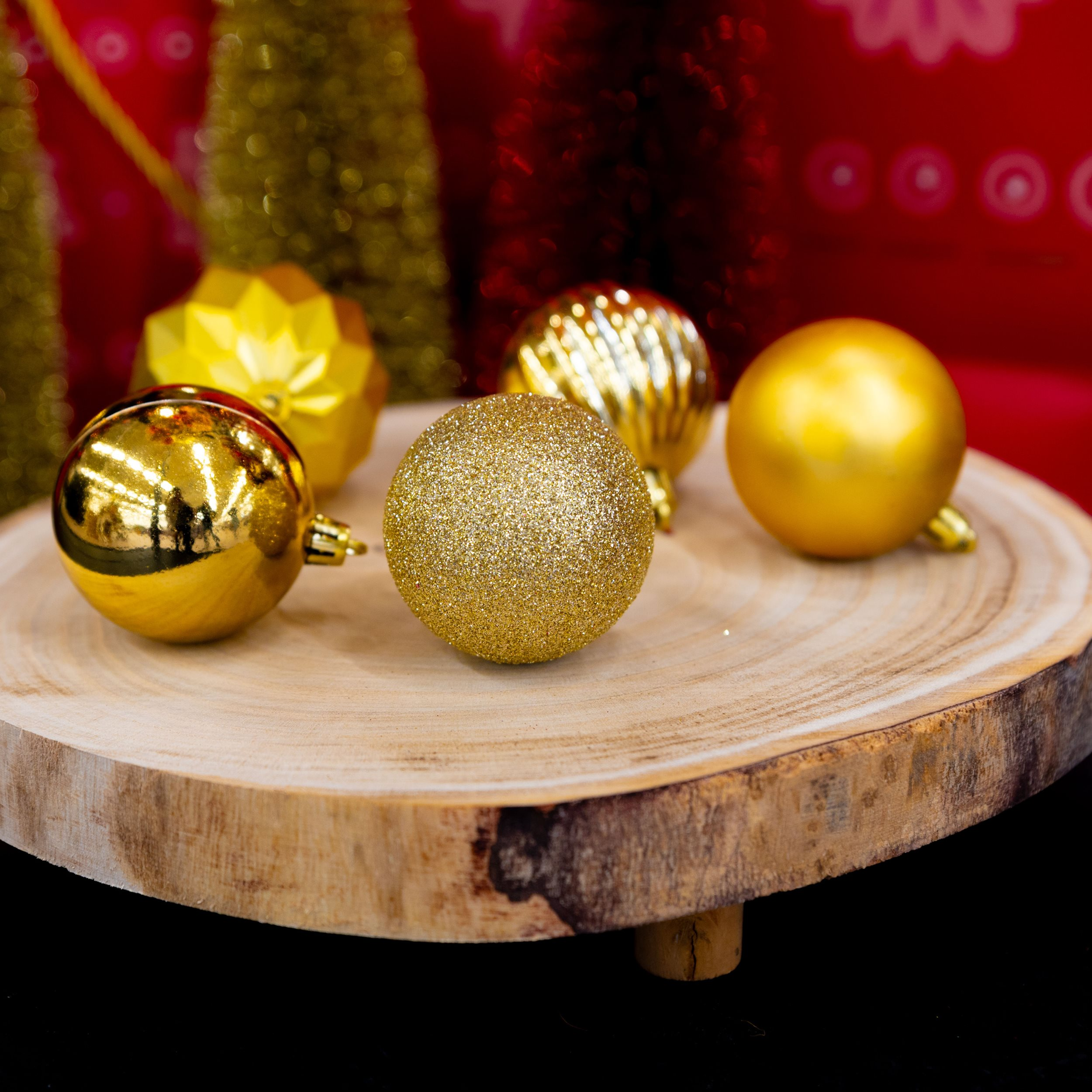 Ornements de Noël dorés sur une tranche de bois, fond rouge avec décorations floues.