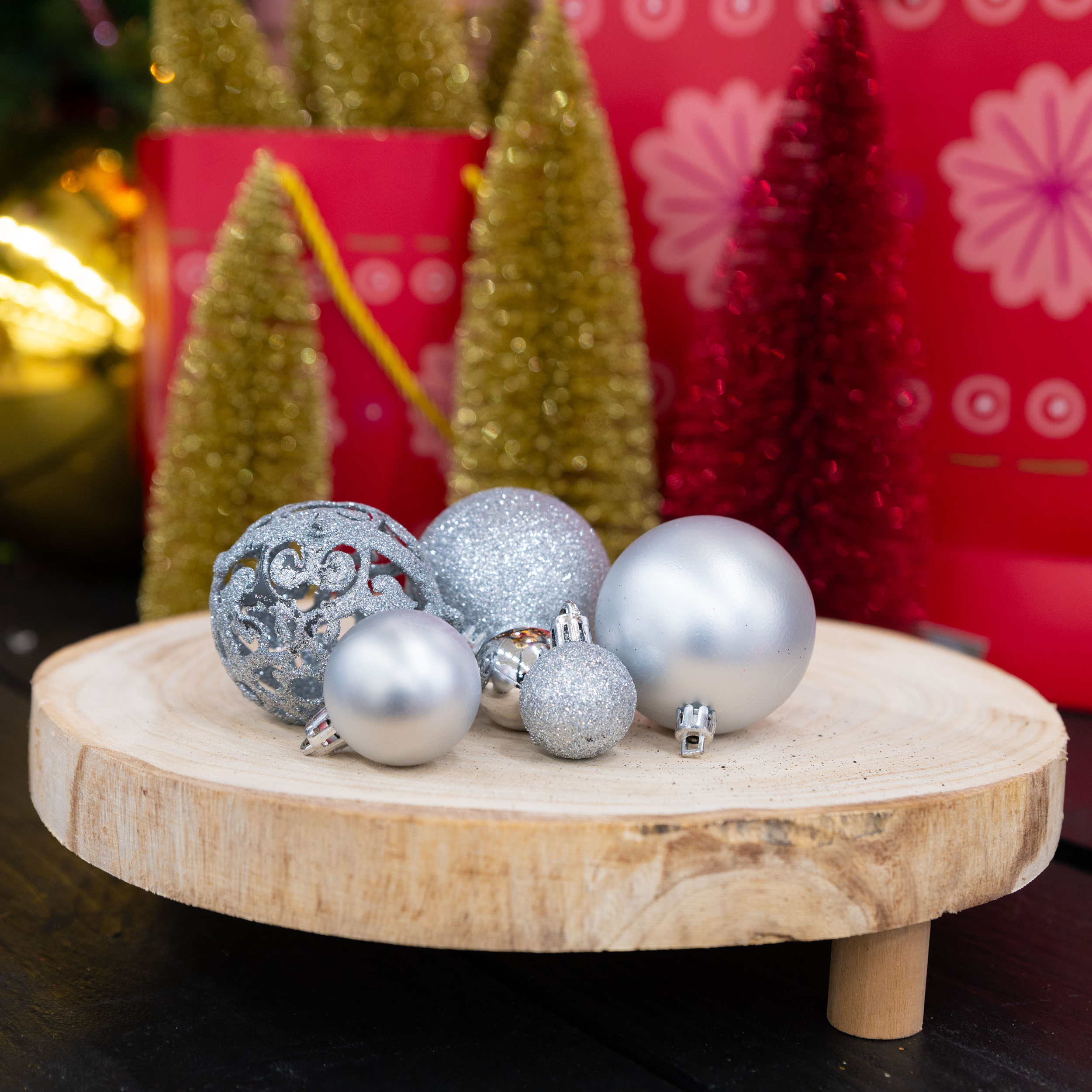 Ornements argentés sur un support en bois. Le fond comprend des arbres de Noël et des décorations rouges et dorées.