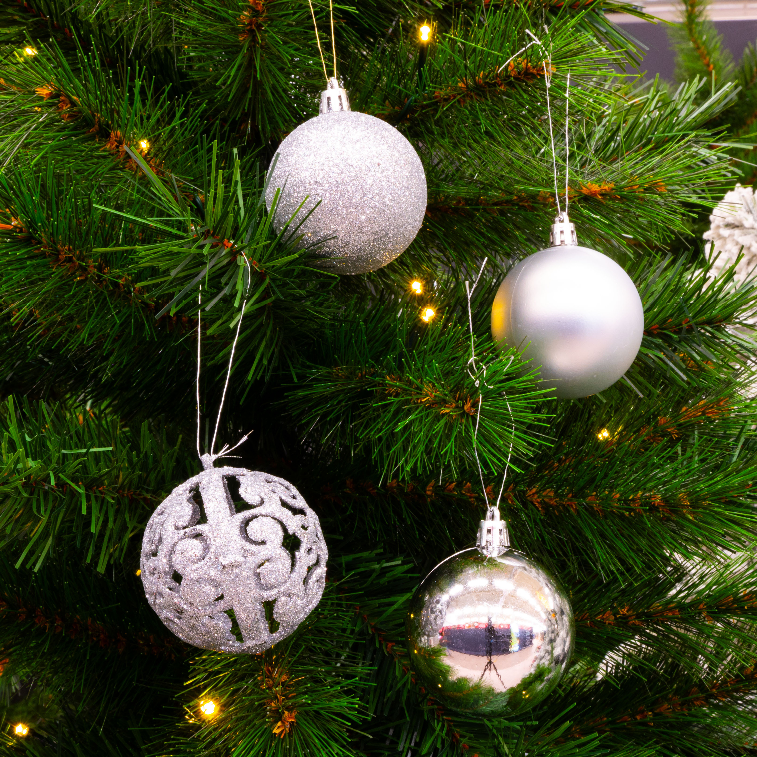 Gros plan sur un arbre de Noël avec des ornements et des lumières argentées. Les aiguilles vertes forment le fond.