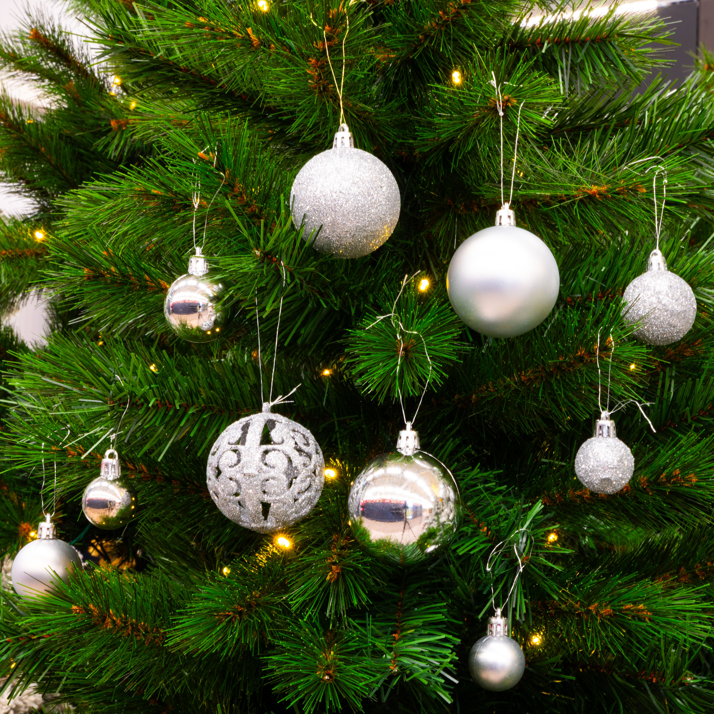 Gros plan d'un sapin de Noël orné de décorations argentées et de petites lumières, sur fond blanc.