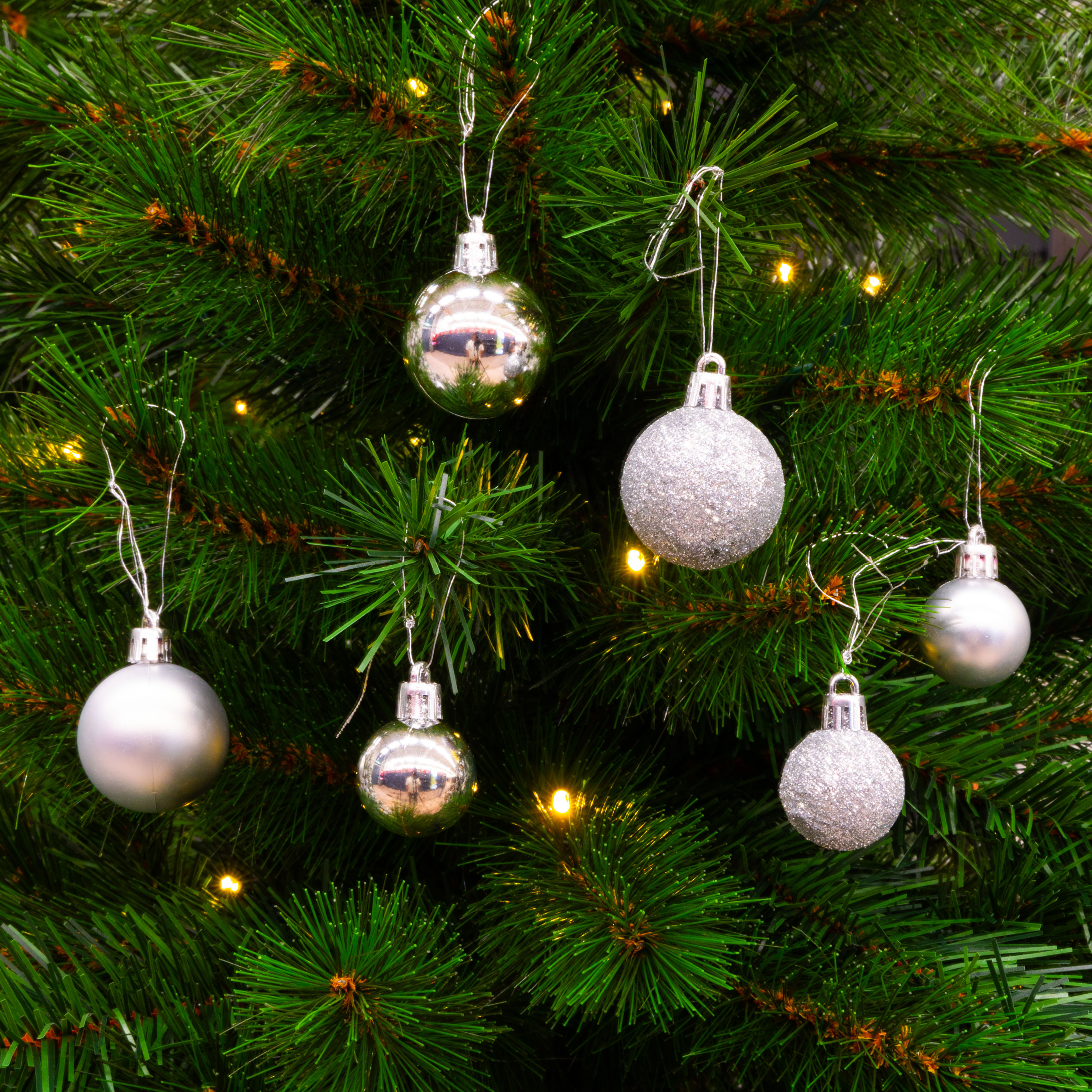 Gros plan d'un sapin de Noël avec des ornements argentés et de petites lumières. L'arbre a des aiguilles vertes.