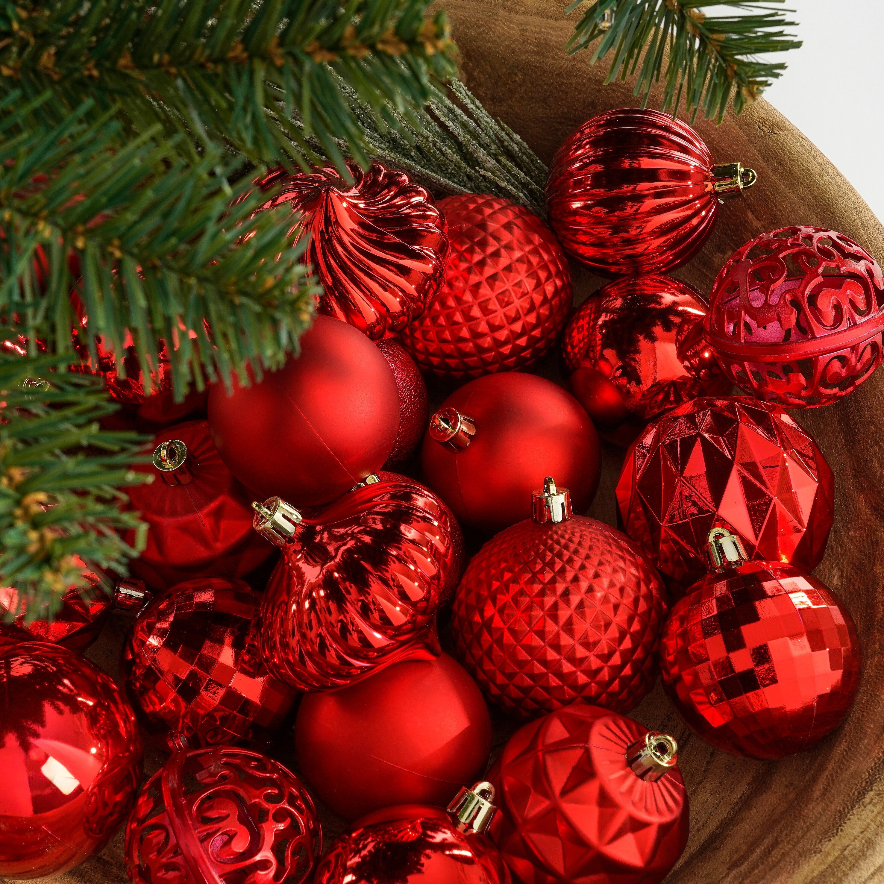Un bol en bois rempli de diverses décorations de Noël rouges, avec des aiguilles de pin vertes en haut.