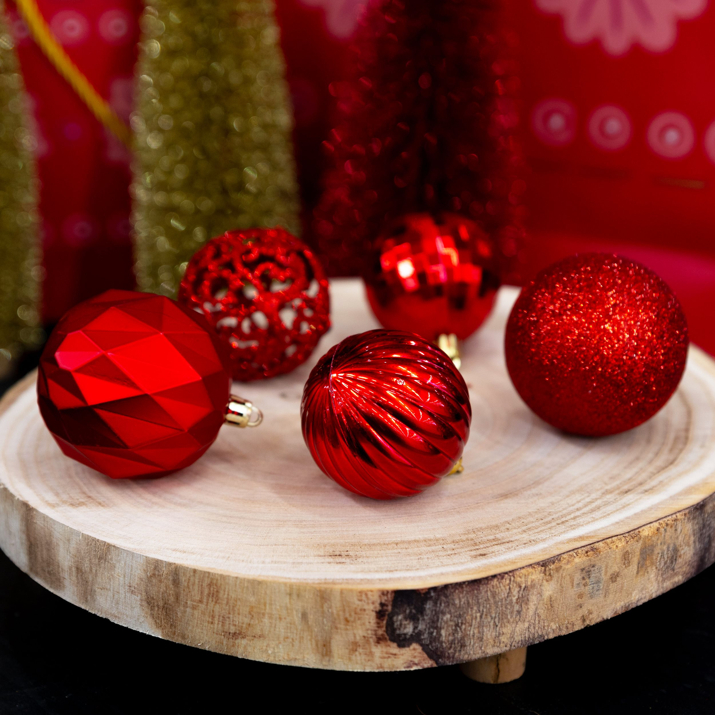 Ornements de Noël rouges sur une tranche de bois, avec des éléments décoratifs verts et rouges en arrière-plan.