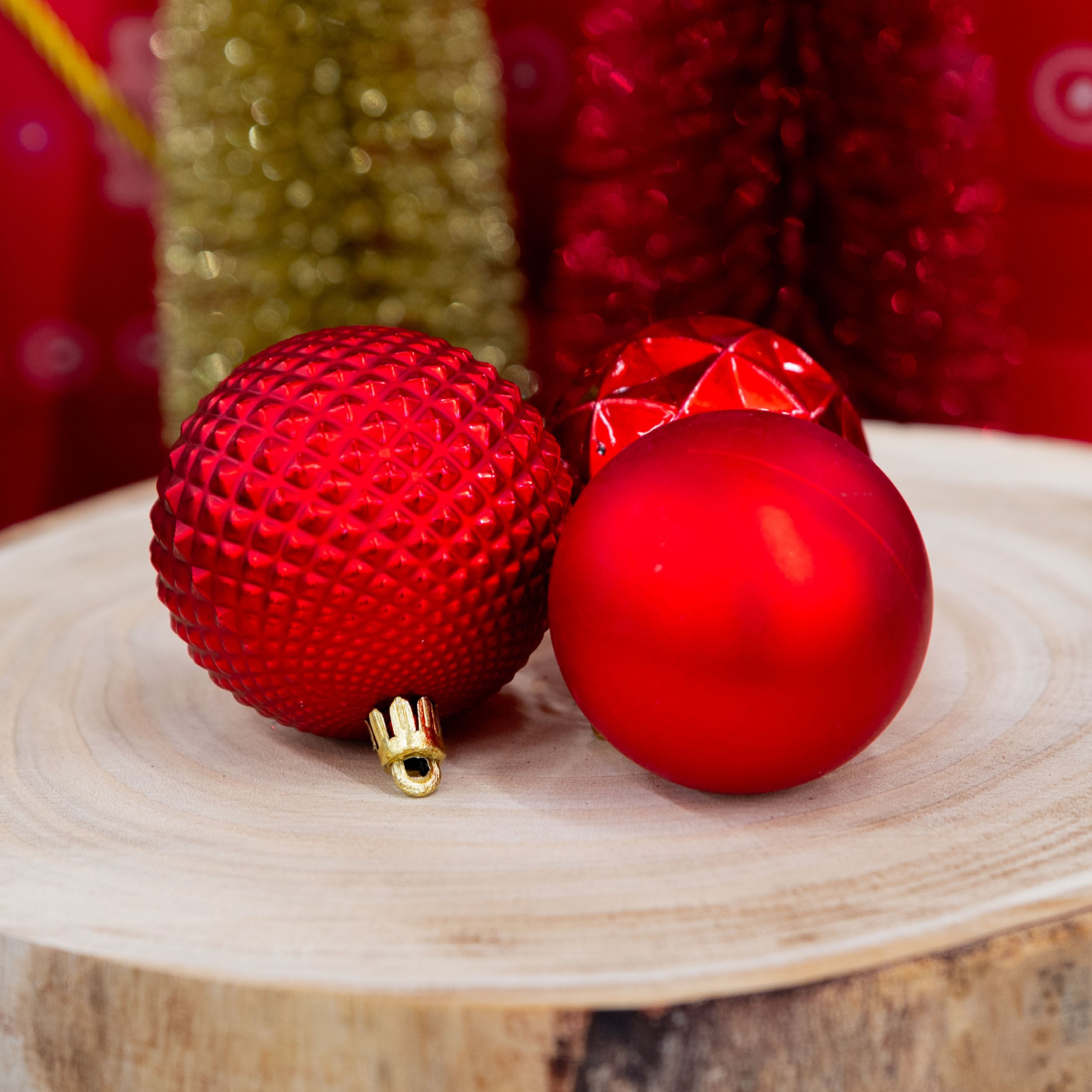 Trois boules de Noël rouges sur une surface en bois, avec des décorations dorées et rouges floues en arrière-plan.