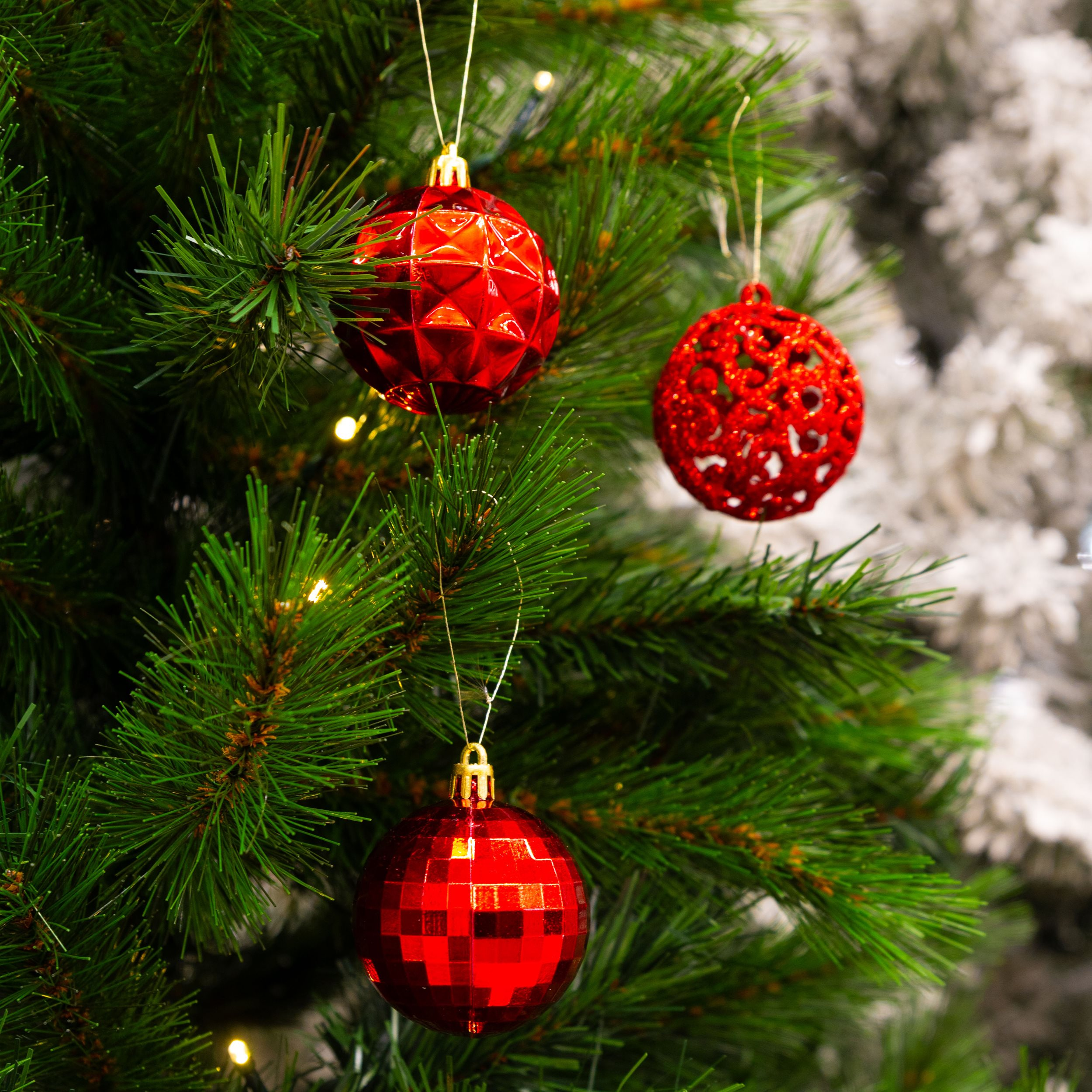 Sapin de Noël avec trois ornements rouges. Aiguilles vertes et fond blanc flou. Les ornements sont suspendus.
