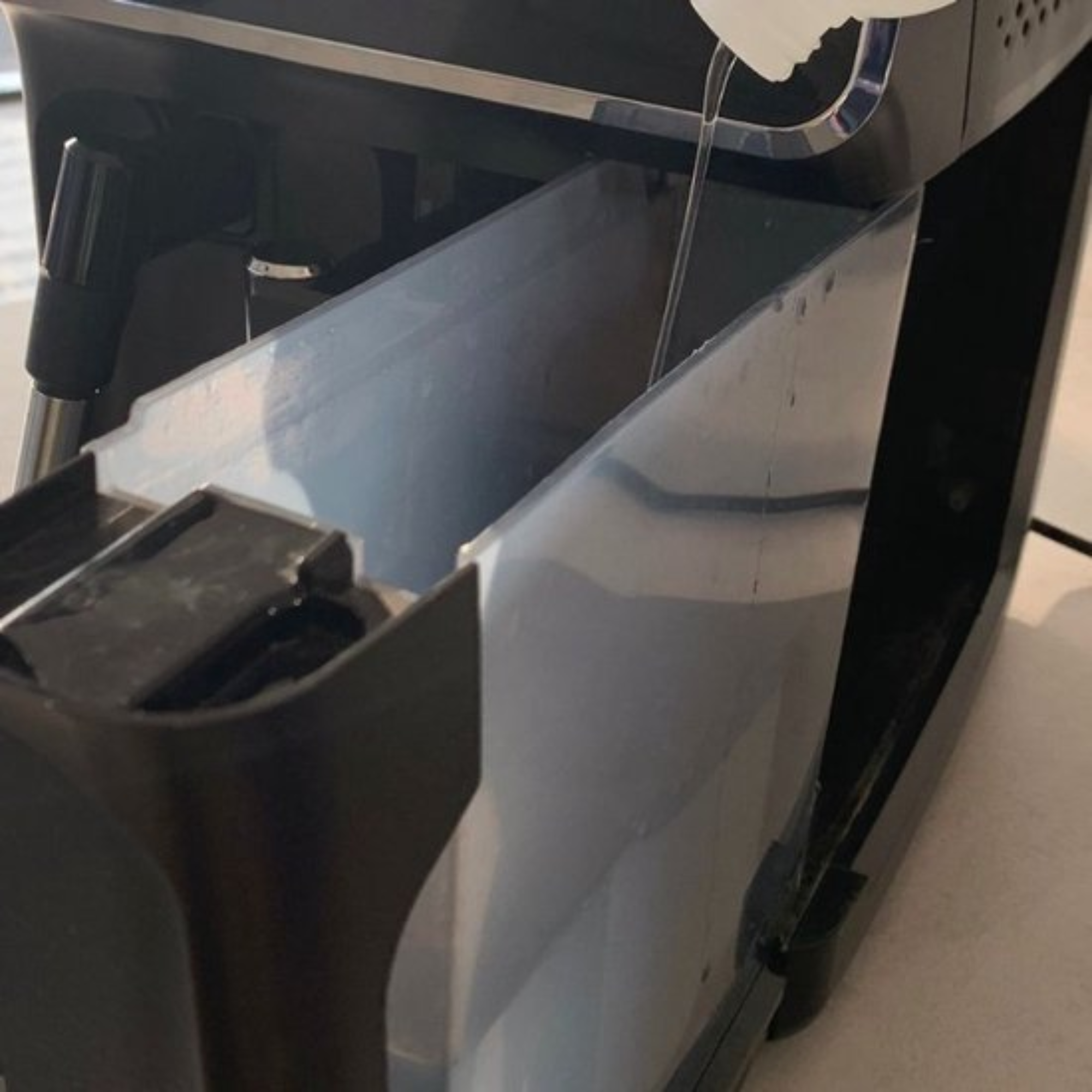 Water is being poured into a transparent reservoir of a black and silver appliance. The scene is indoors.
