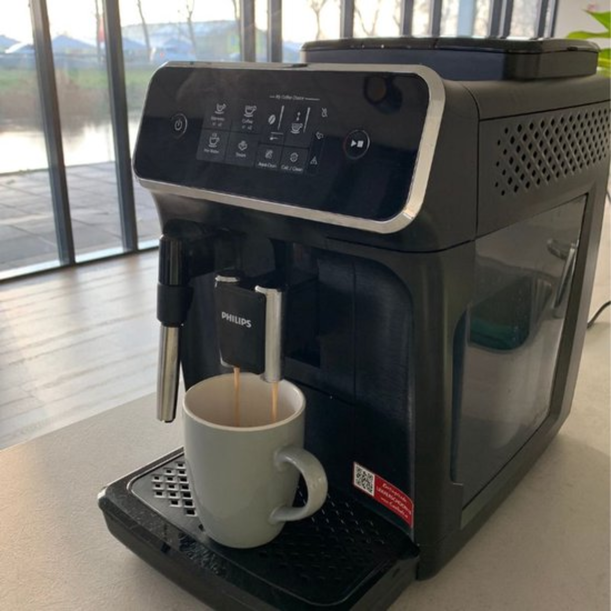 A Philips espresso machine brewing coffee into a gray mug. The machine is black and sits on a counter.