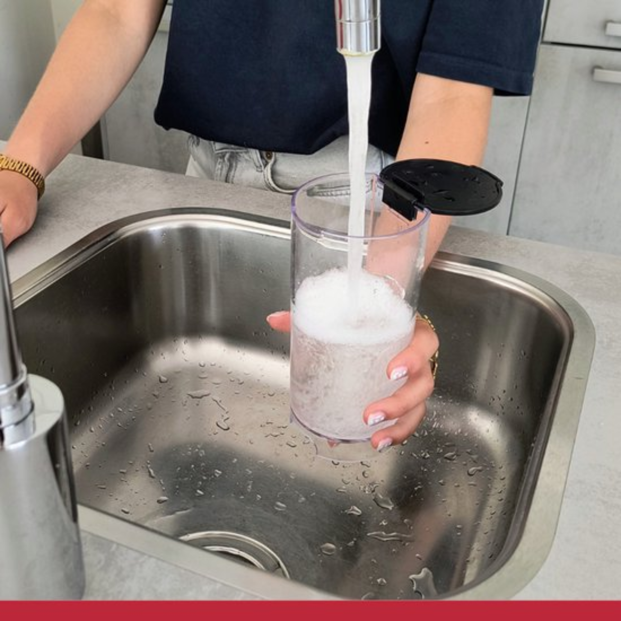 A person fills a clear cup with water from a faucet in a stainless steel sink. The cup is nearly full.