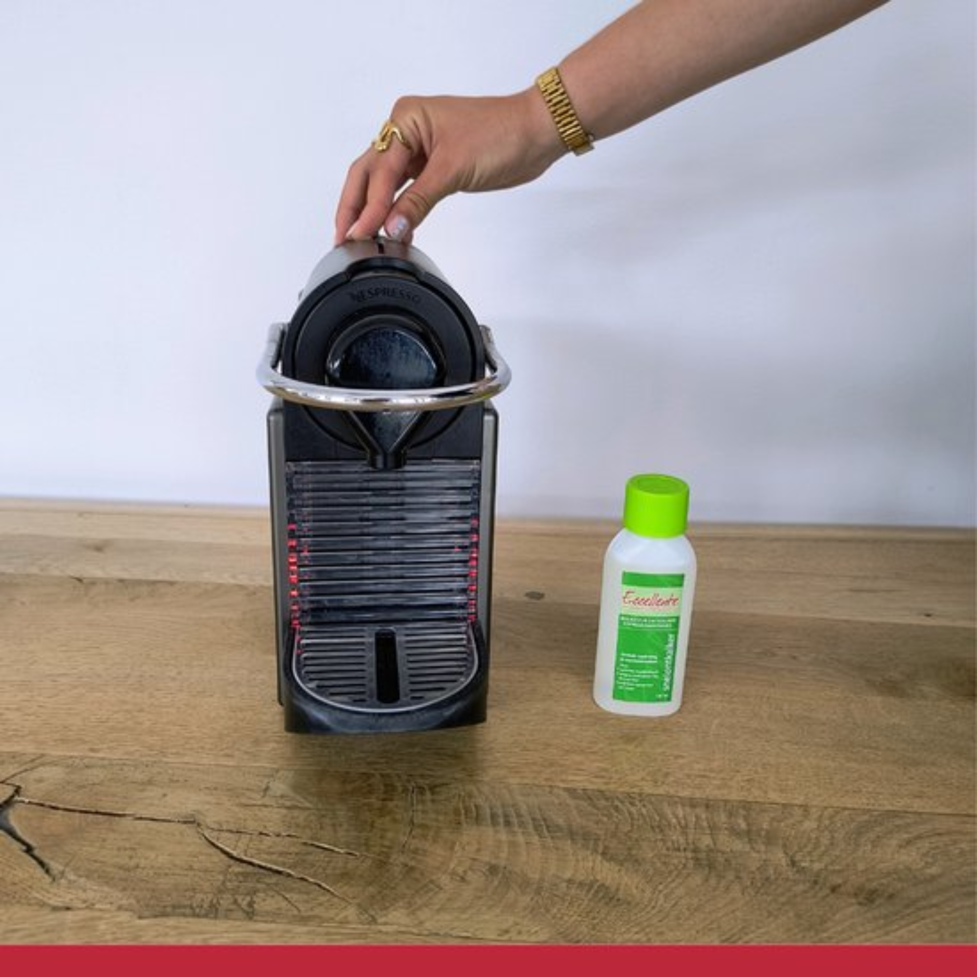 A hand touches a black Nespresso machine. A bottle of descaler stands next to it on a wooden surface.